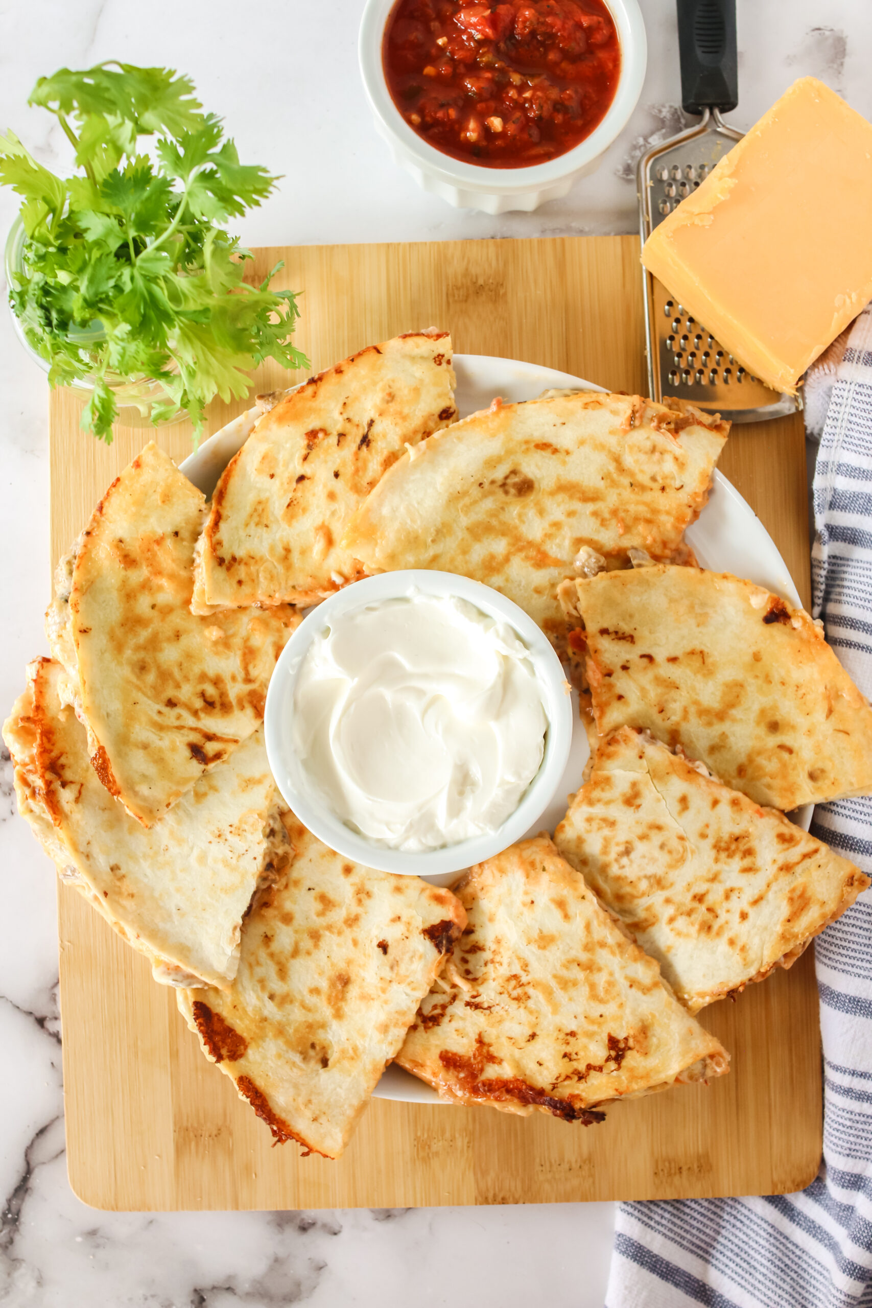 2 quesadillas cut and placed on a platter with a bowl sour cream