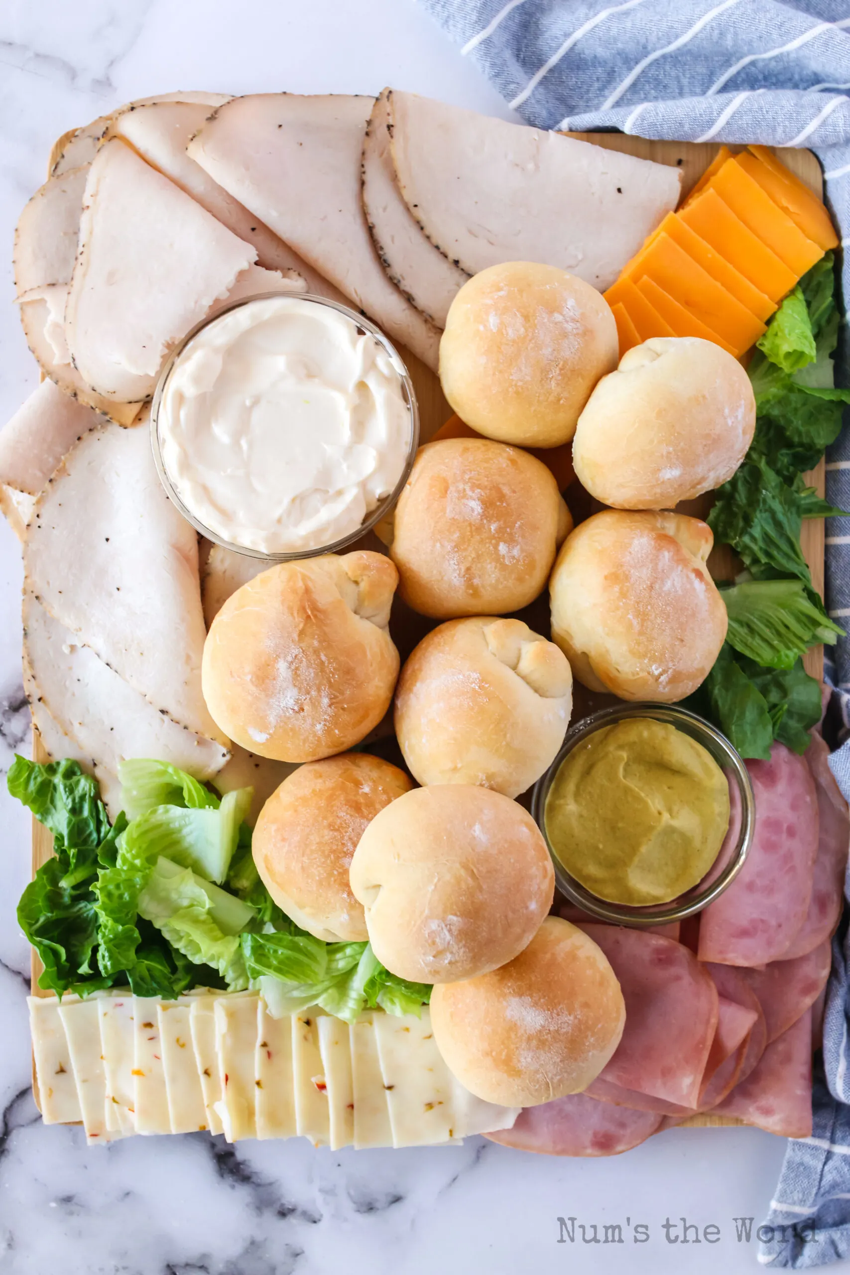 zoomed out image of sandwich charcuterie board with buns, meats, cheeses and spreads. board.