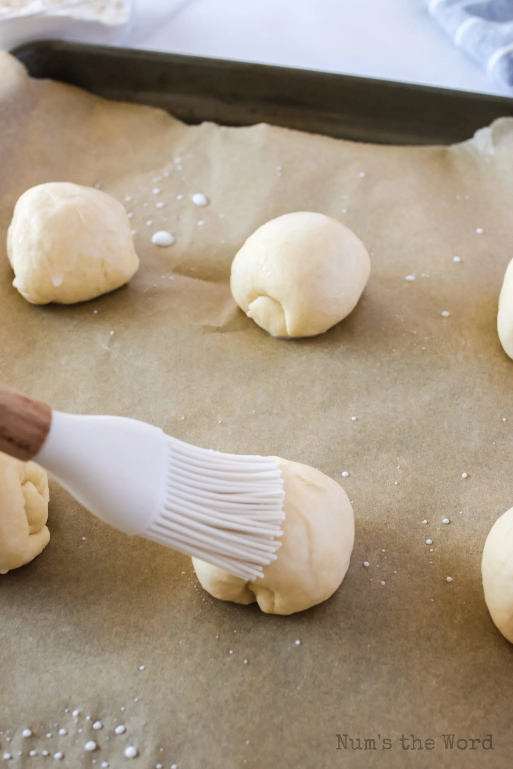 butter being brushed onto rolls before baking.