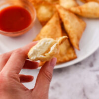 hand holding a cream cheese wonton that is cut in half to show cream cheese filling