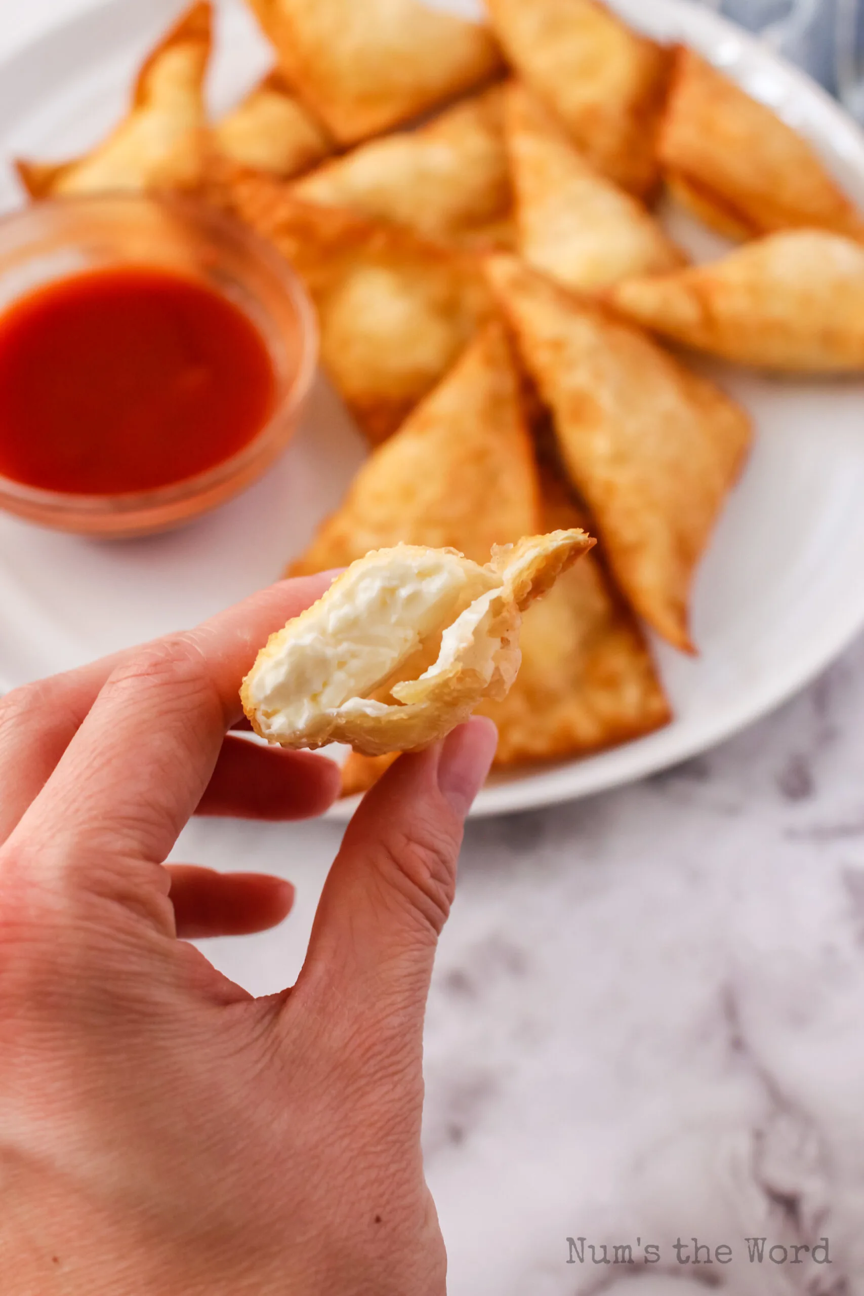 hand holding a cream cheese wonton that is cut in half to show cream cheese filling