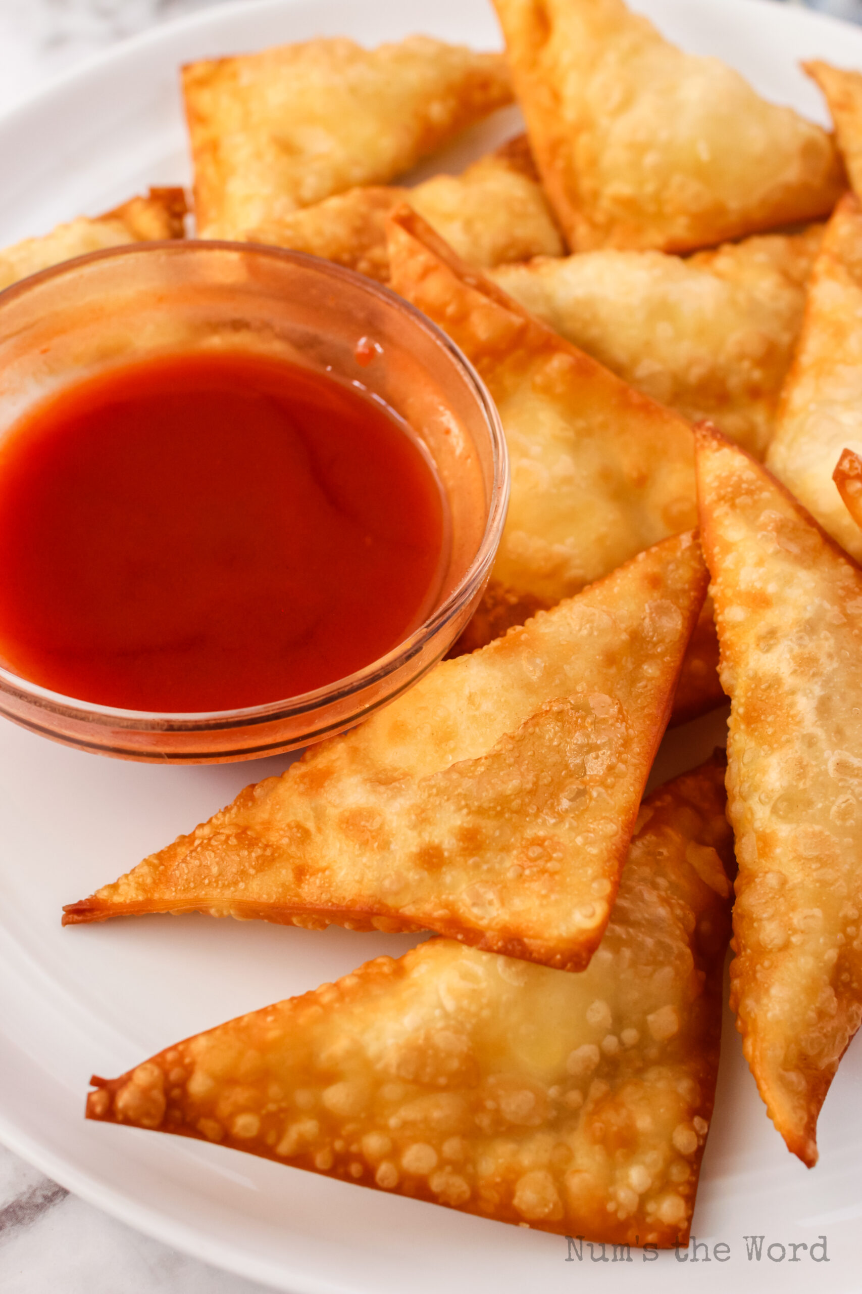 close up side view of cream cheese wontons on platter with dipping sauce