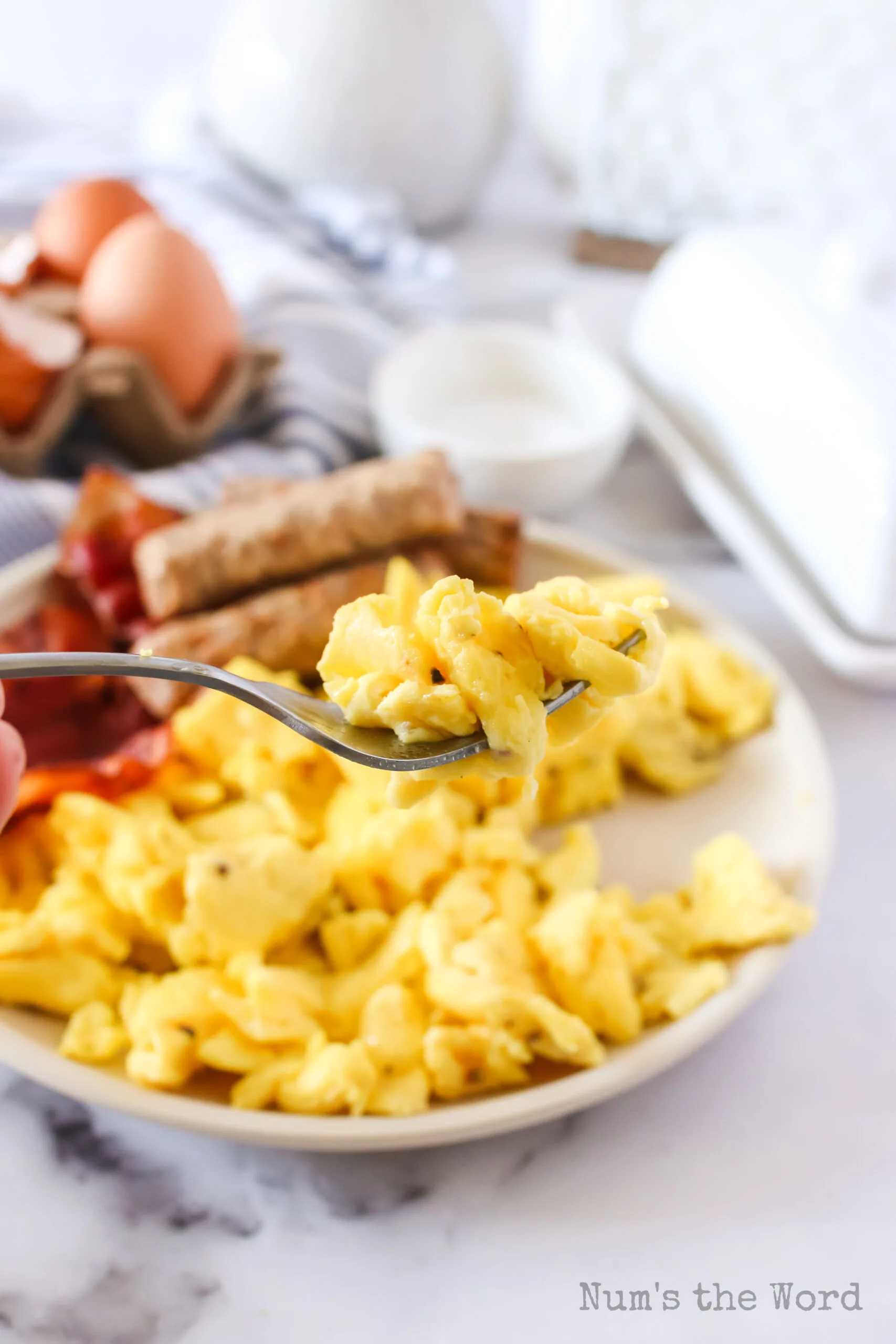 plate full of scrambled eggs. Fork being held above full of eggs.