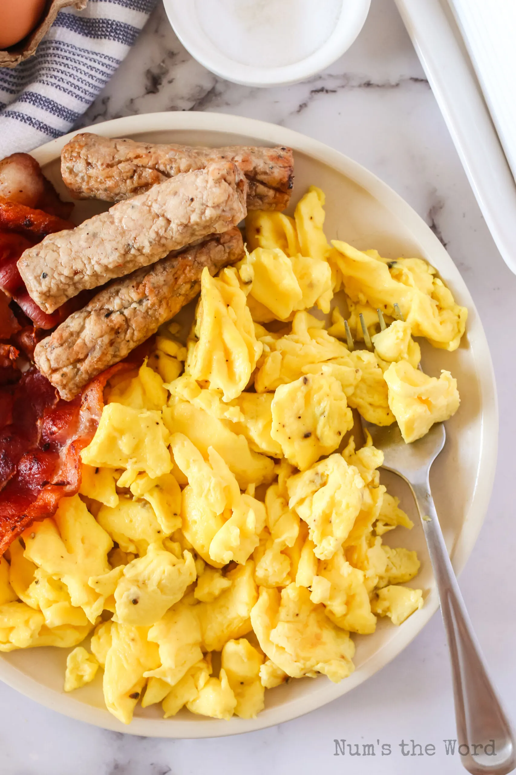 plate full of eggs and bacon and sausage with a fork in the eggs