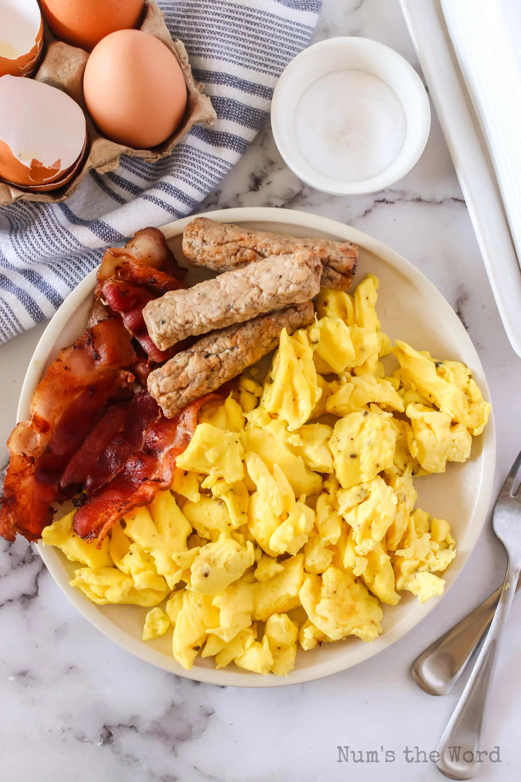 zoomed out image of cooked eggs on a plate with bacon and sausage