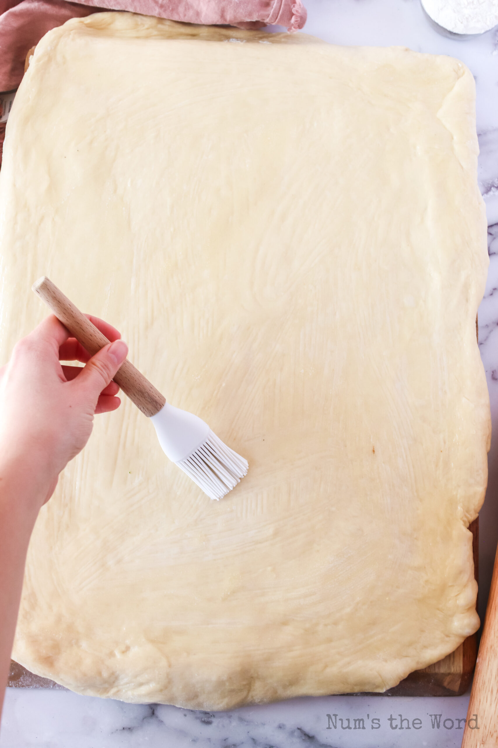 dough rolled out into a rectangle with melted butter being brushed over the surface.