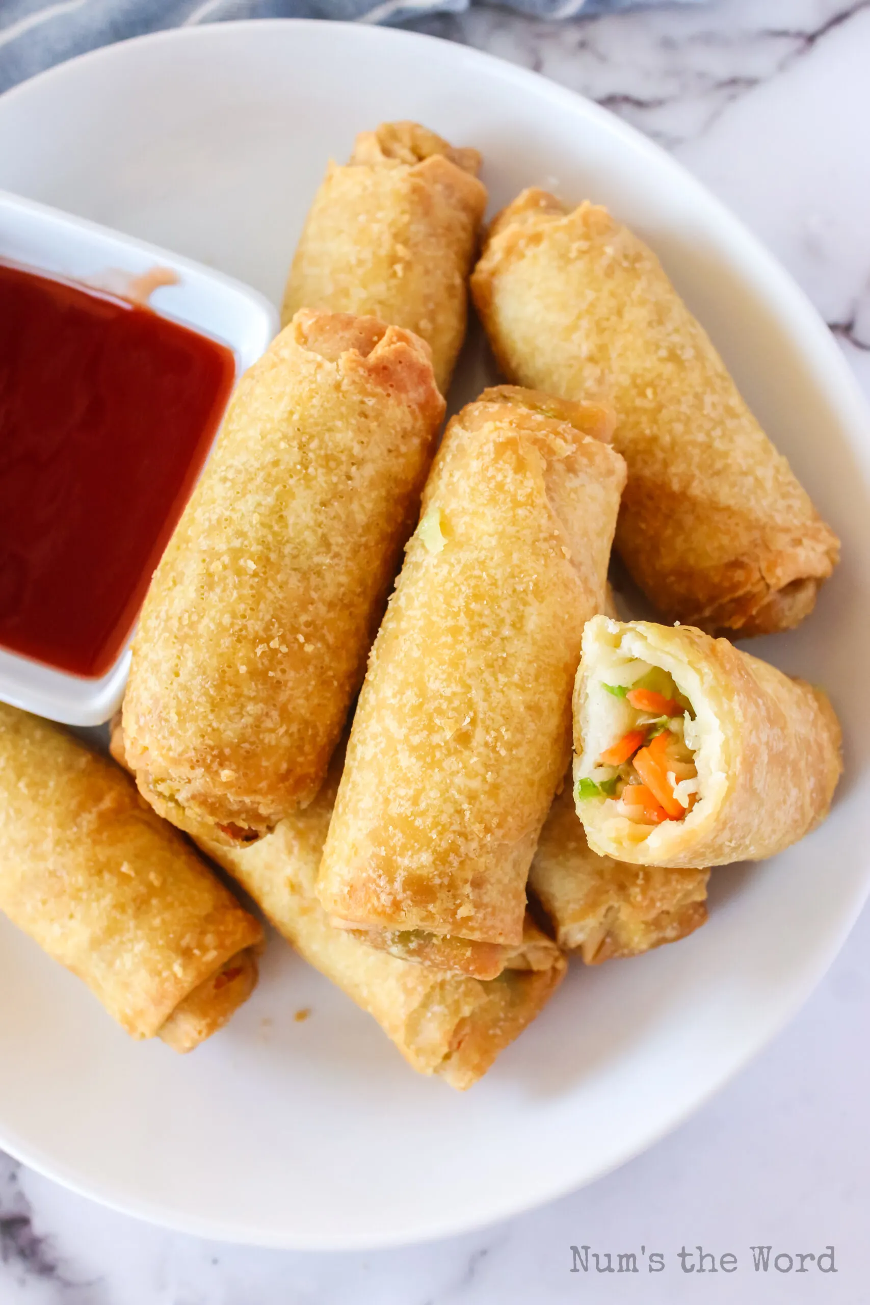 egg rolls on plate with dipping sauce. One egg roll cut in half to show filling.