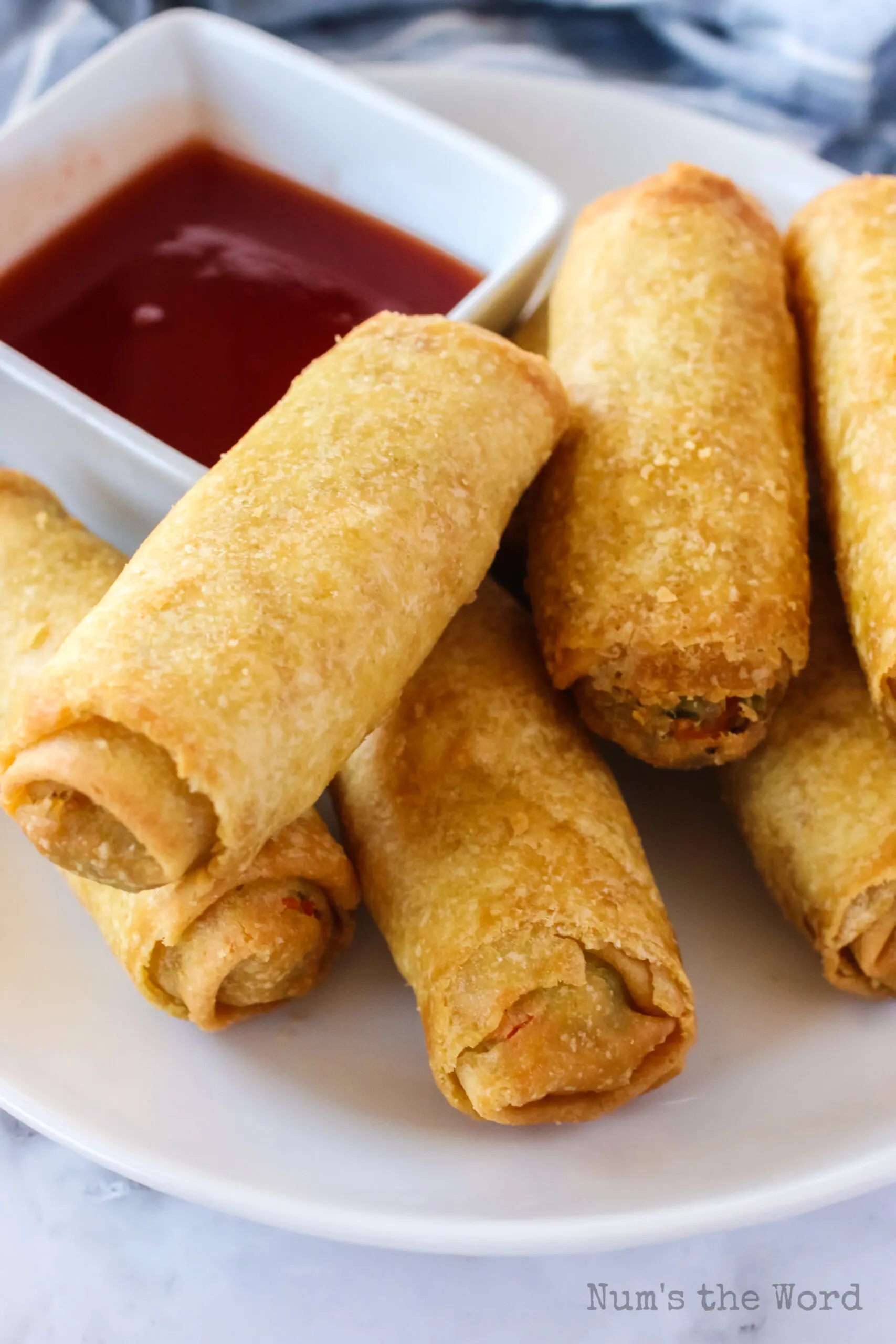 zoomed in image of cooked egg rolls with bowl of sweet and sour sauce.