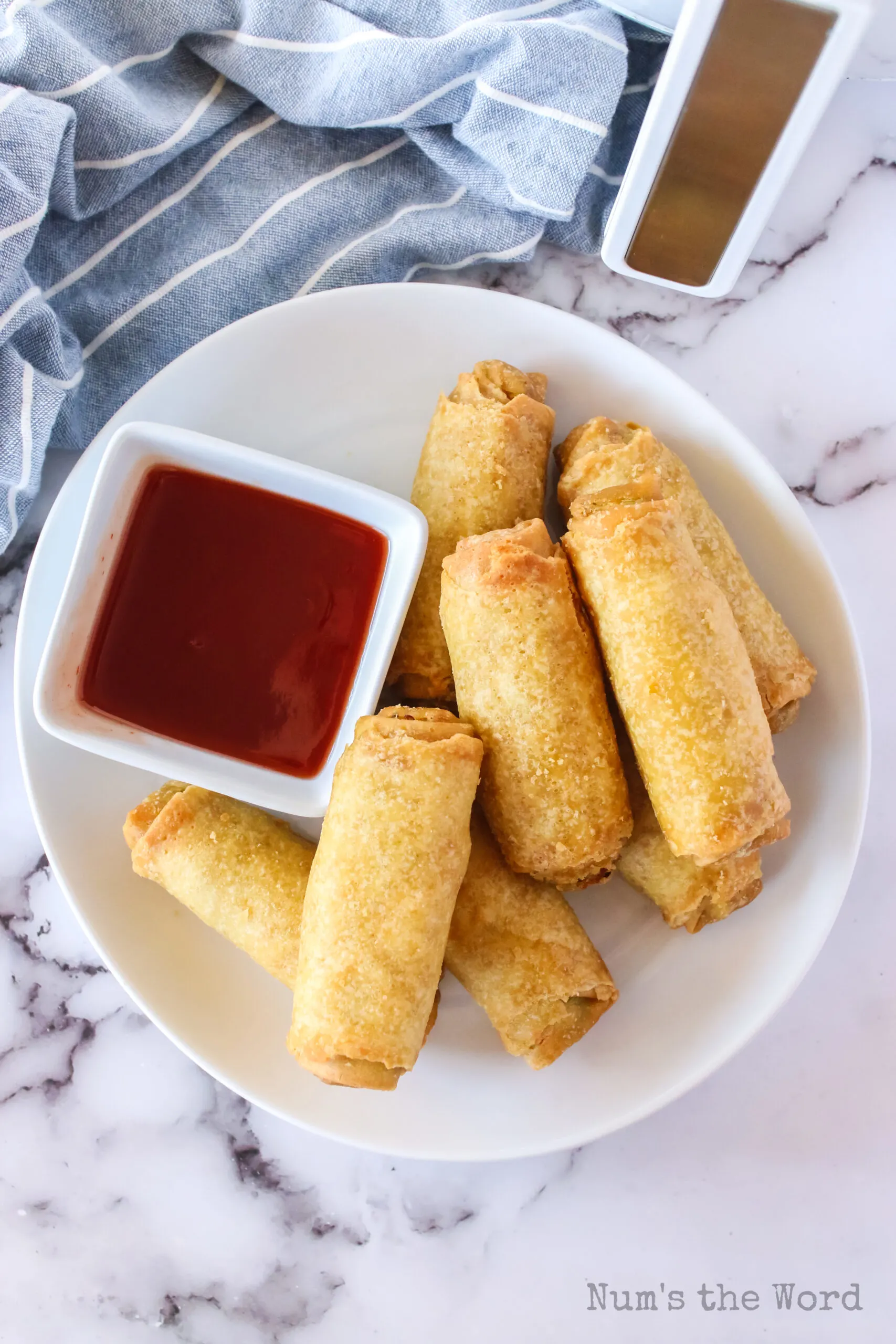 zoomed out image of cooked egg rolls on a plate with sweet and sour sauce in a small bowl