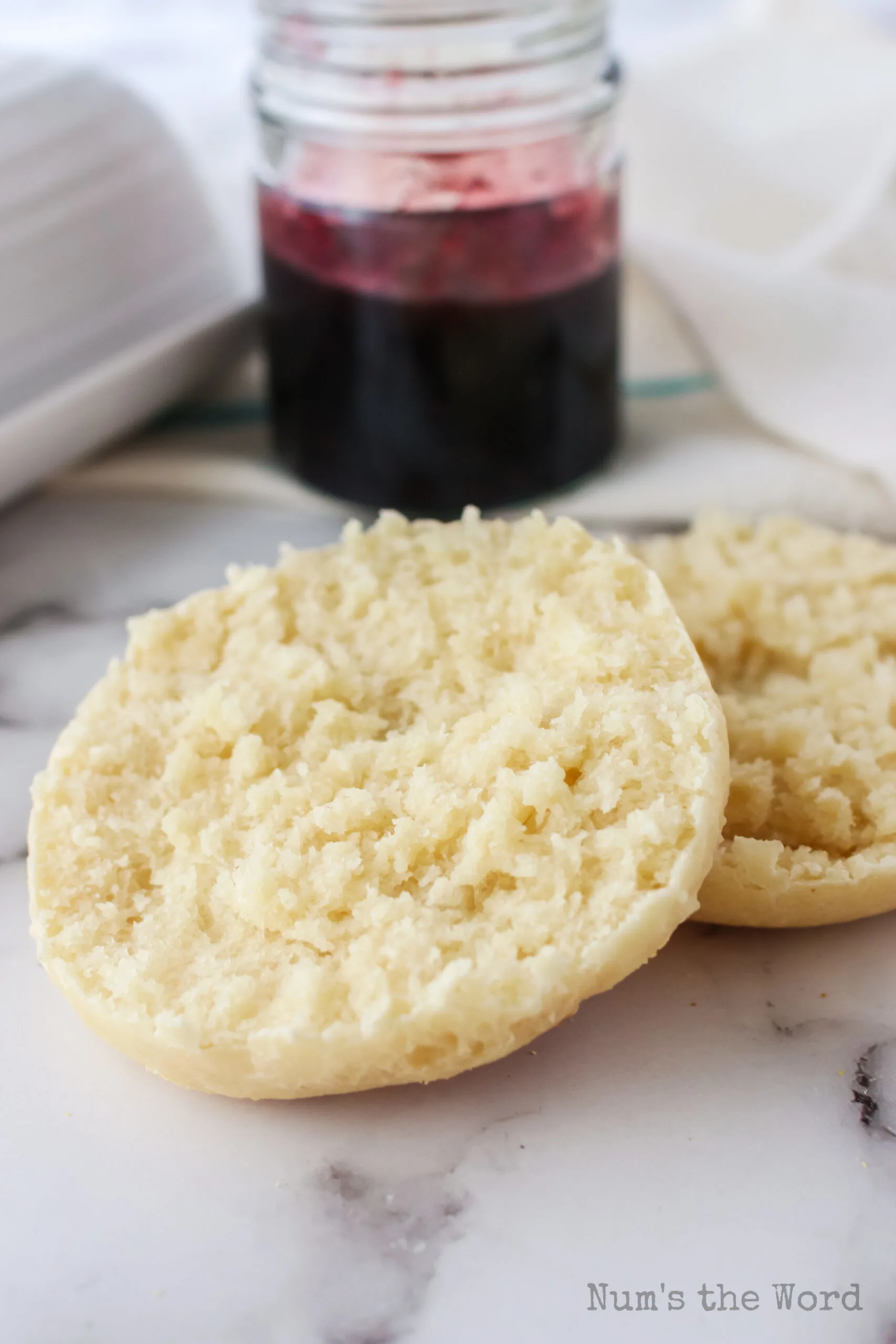 side view of english muffin split with jam in the background.