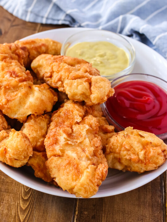 Fried chicken tenders on a plate with honey mustard and ketchup
