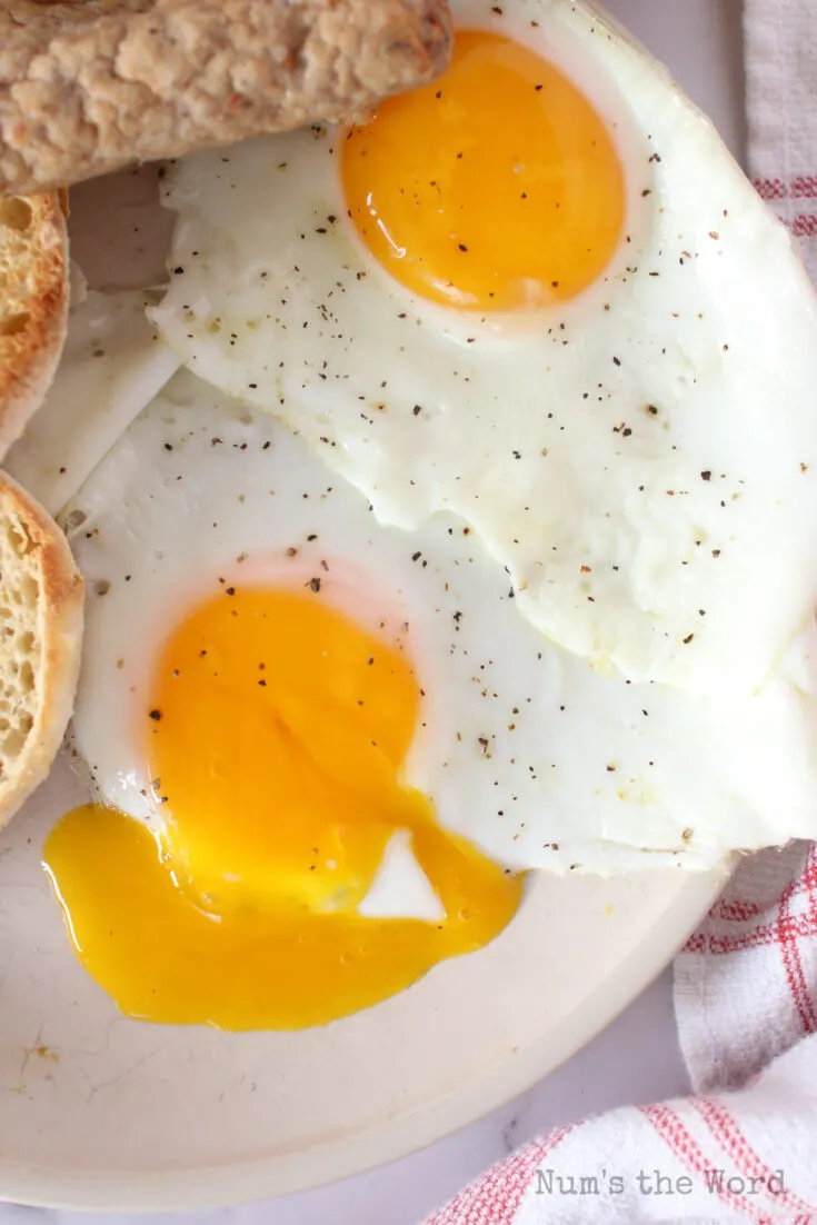 two cooked eggs on plate with one of the egg yolks split to show yummy insides.