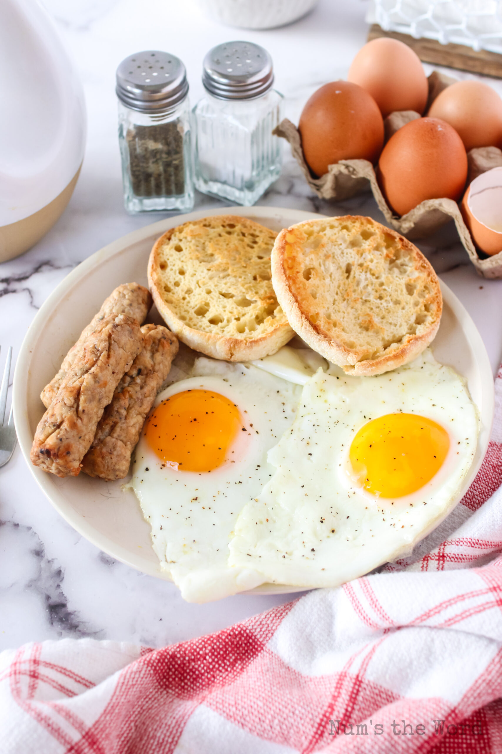 zoomed out image of eggs on a plate with english muffins and sausage links