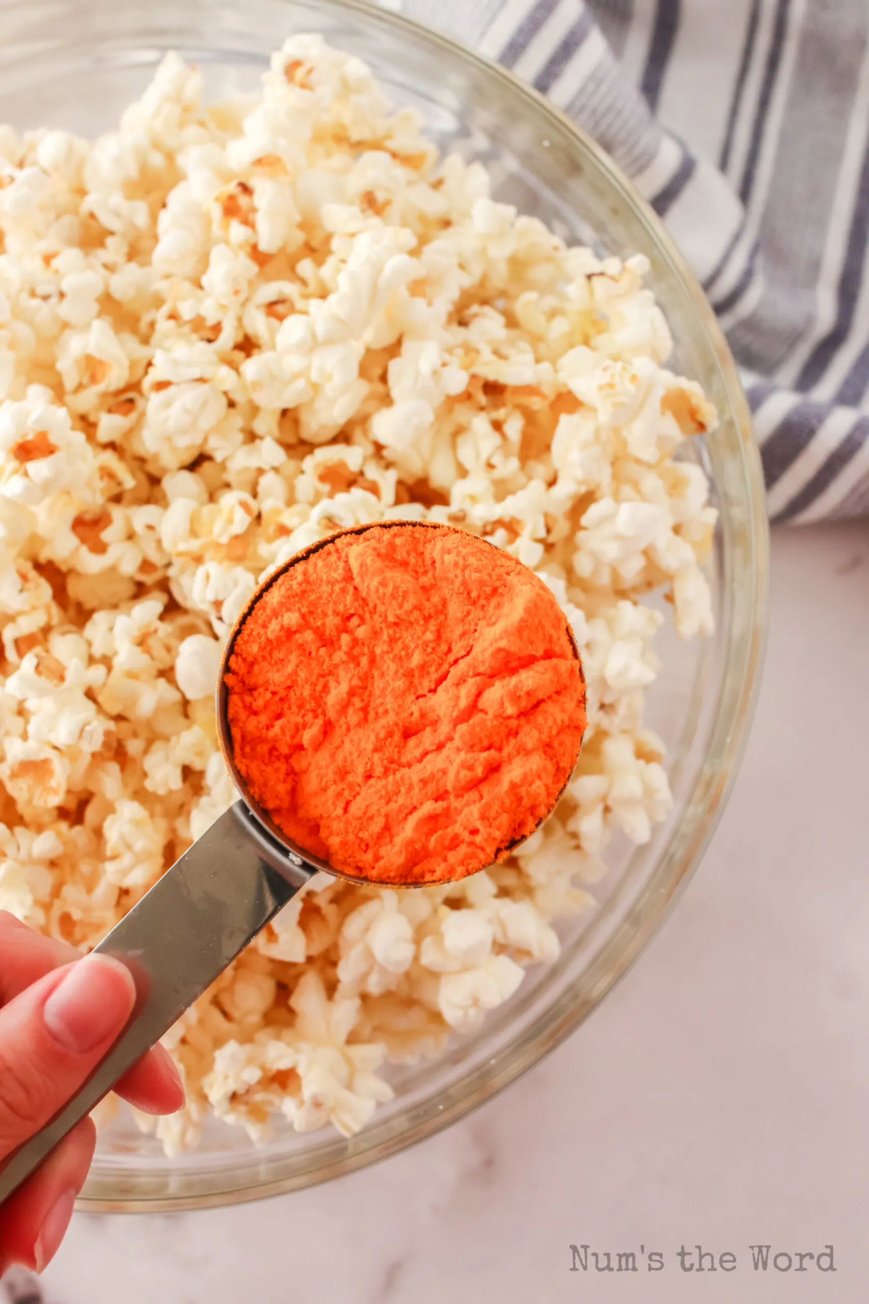 Yellow cheese powder in a measuring cup held over popcorn