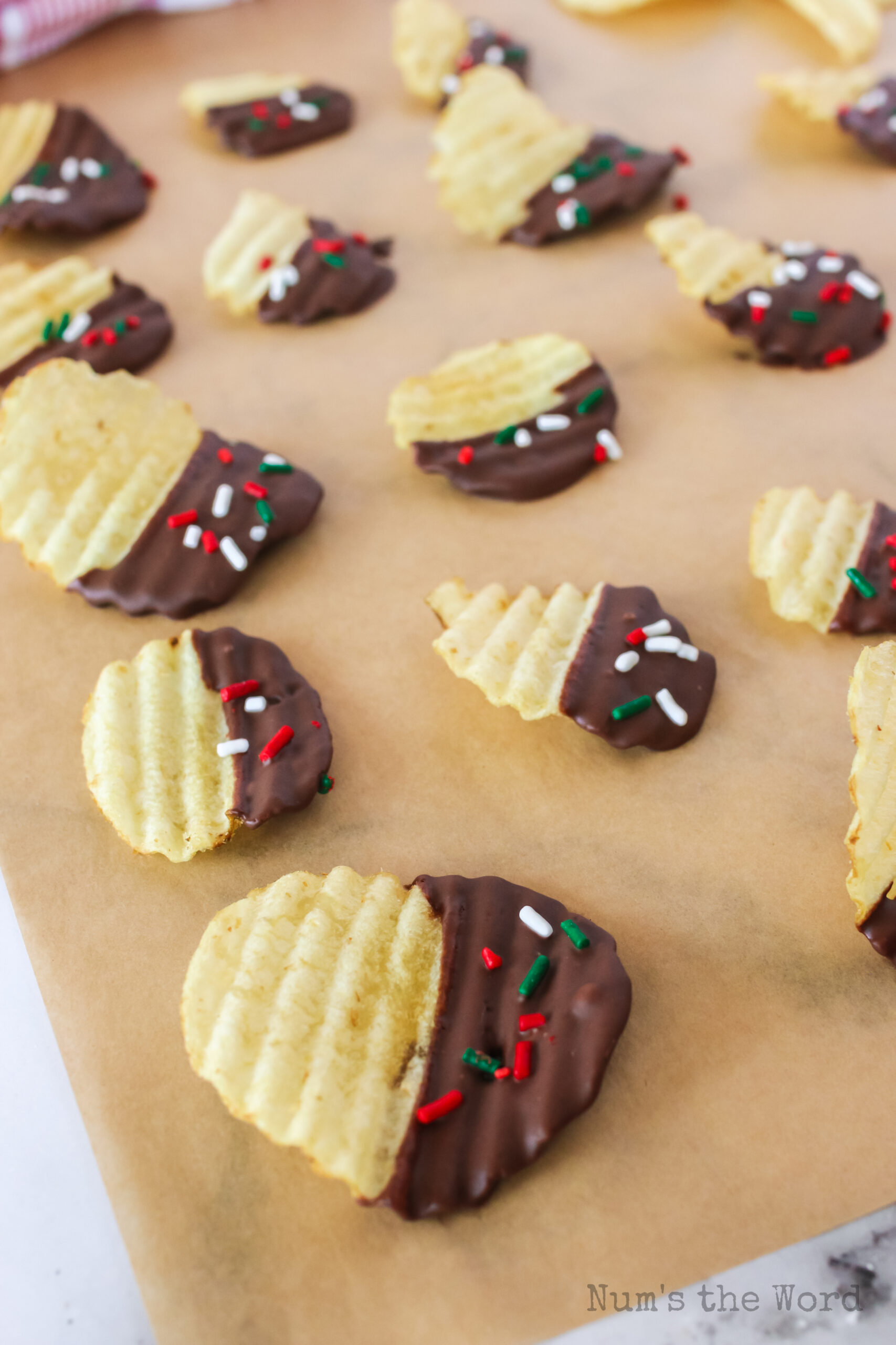 chocolate potato chips dipped with red and green sprinkles on parchment paper.