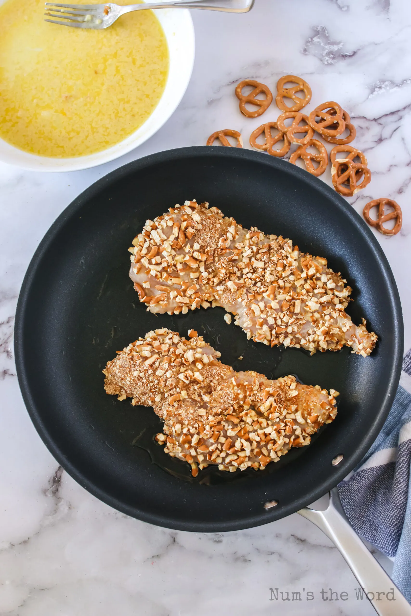 two chicken breasts covered in pretzels in a skillet