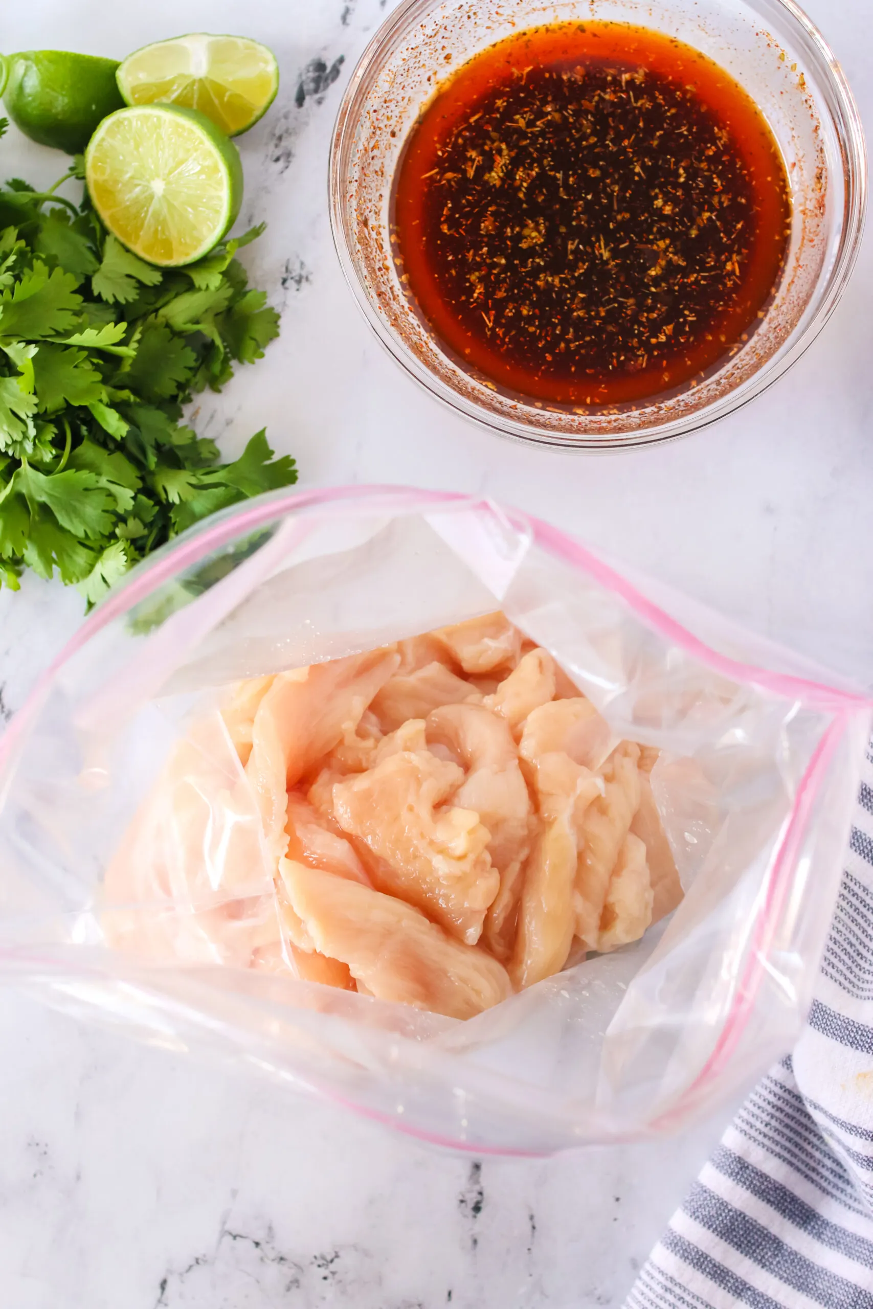 cut up chicken in a ziploc bag with a bowl of marinade in bowl, ready to pour into chicken.