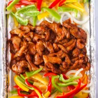 marinade chicken poured onto sheet pan with onions and bell peppers on either side.