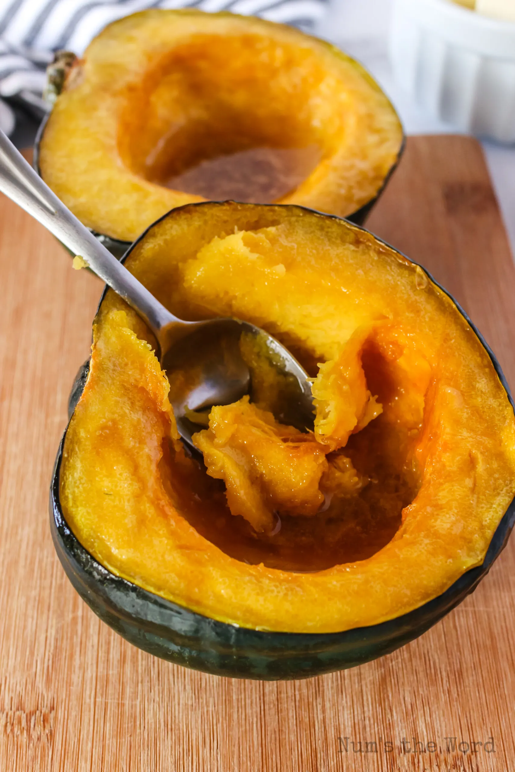 two squash halves on wooden board with a fork scooping out a cooked bit