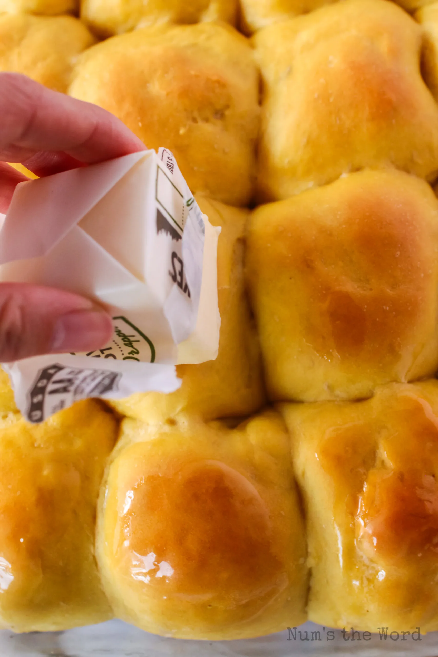 hand holding a stick of butter and buttering the rolls