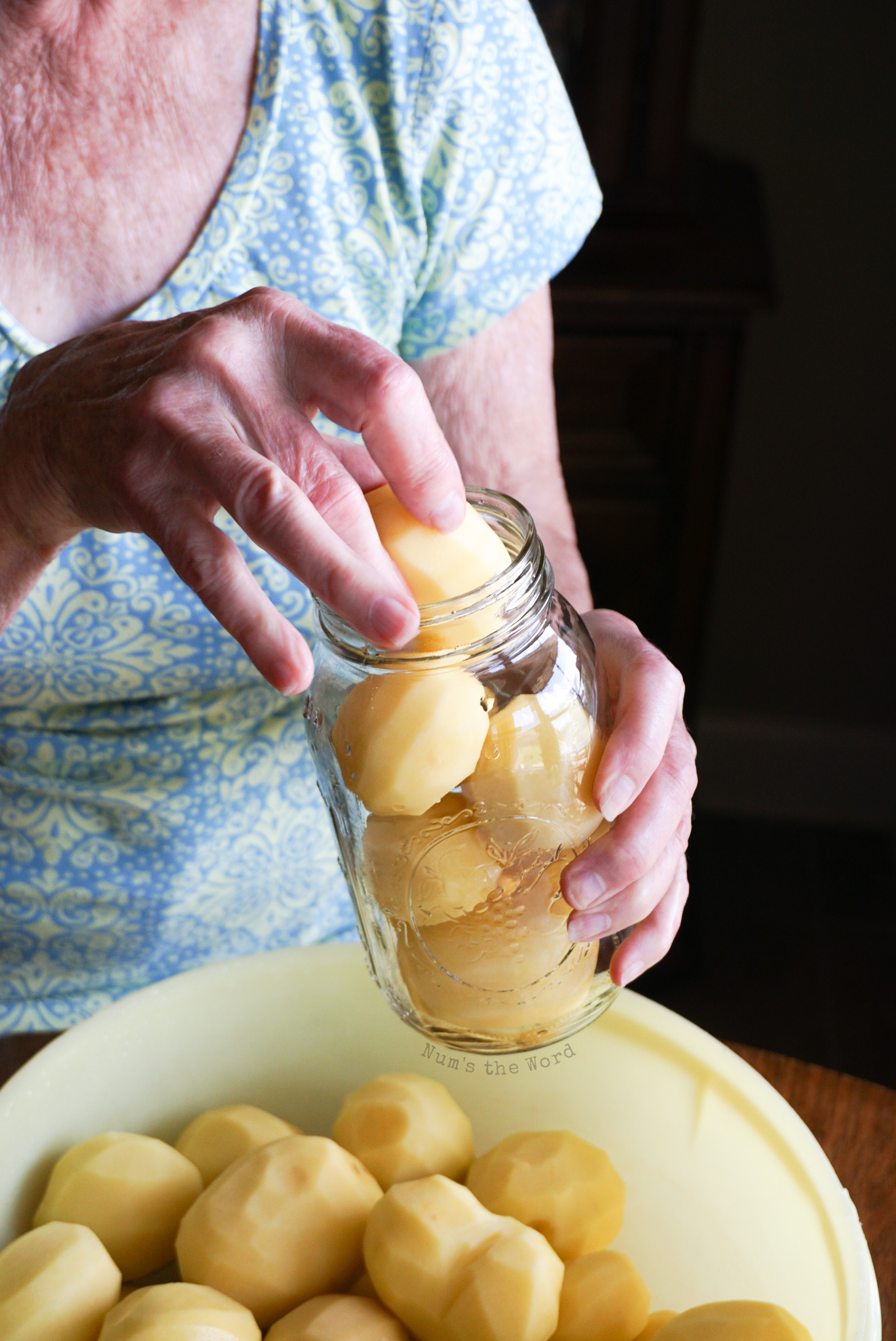 hand filling a quart jar with whole peeled potatoes