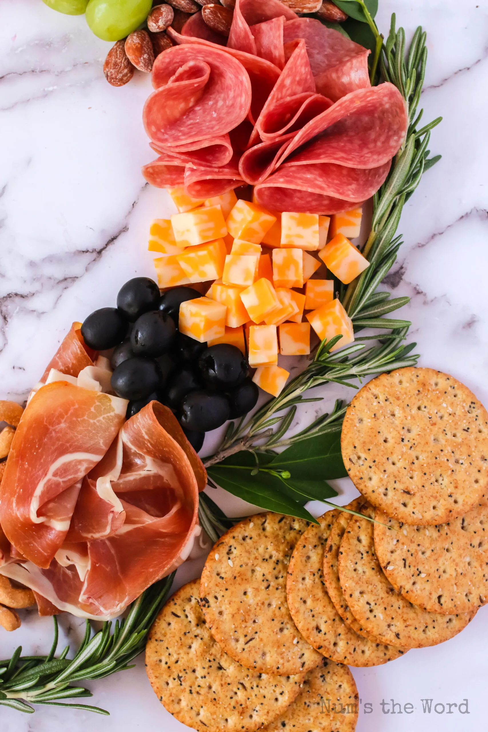 zoomed in image of crackers, salami, cheese, olives and prosciutto