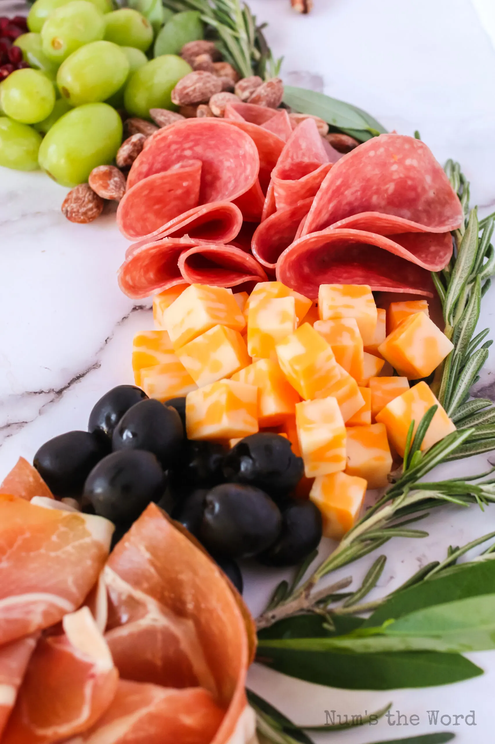 zoomed in image of prosciutto, black olives, cheese, salami, green grapes and almonds