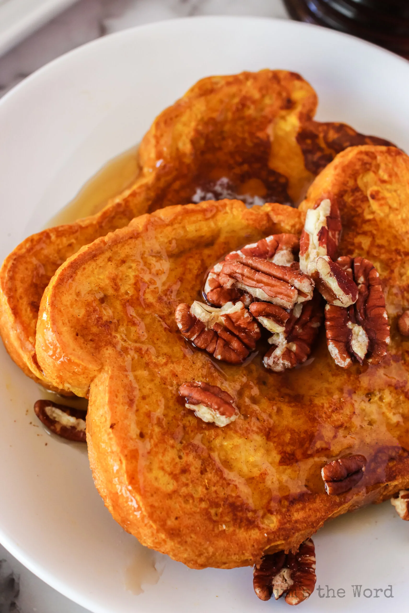 two slices of french toast on plate with syrup and pecans