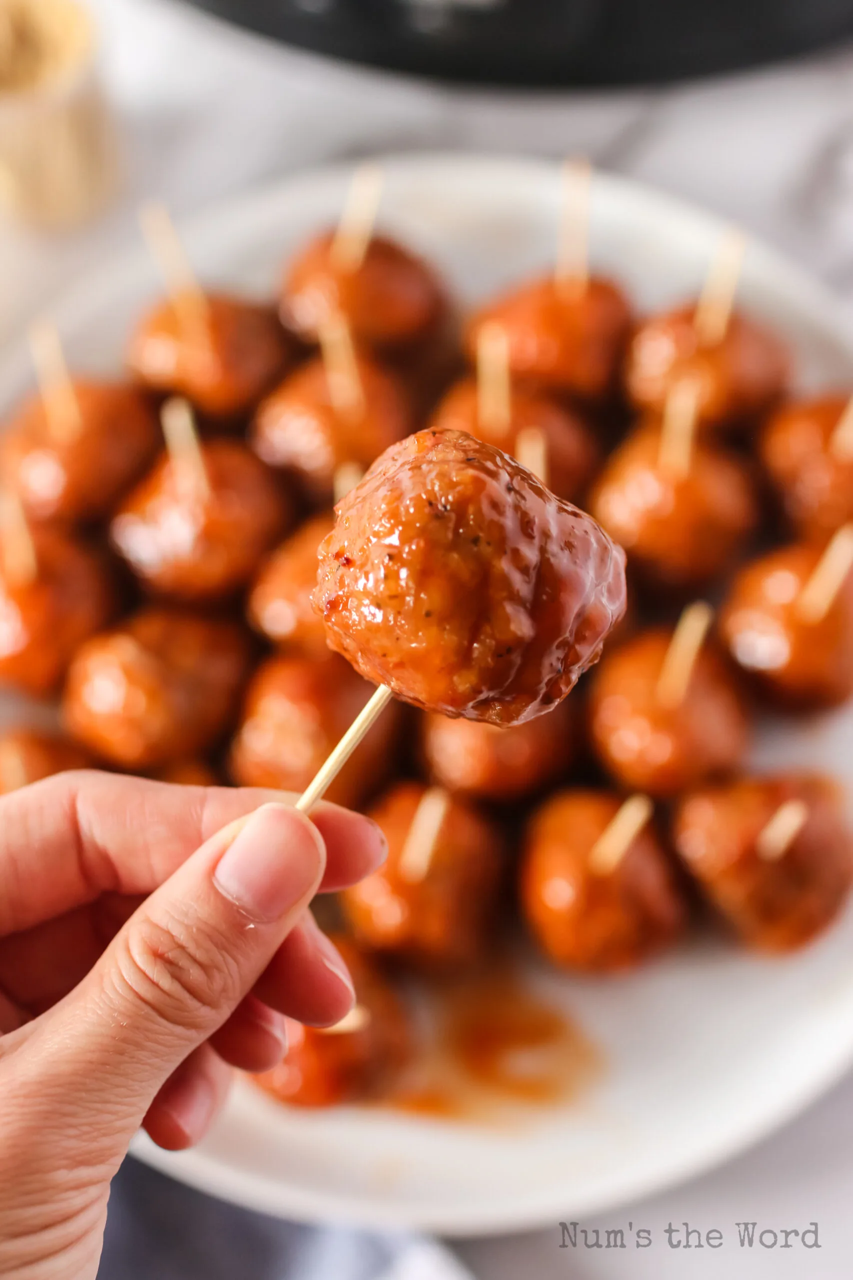 hand holding a single meatball with a toothpick as an appetizer