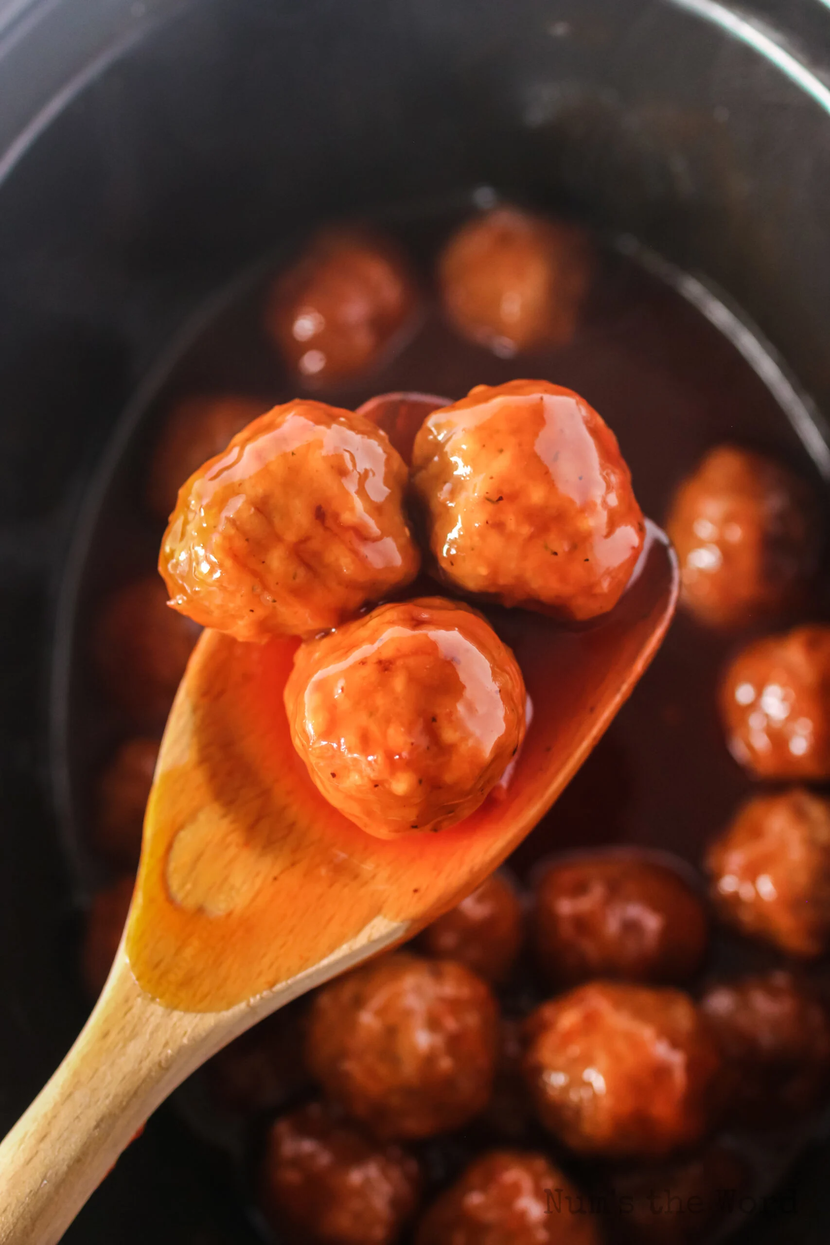 spoon holding up 3 meatballs on wooden spoon