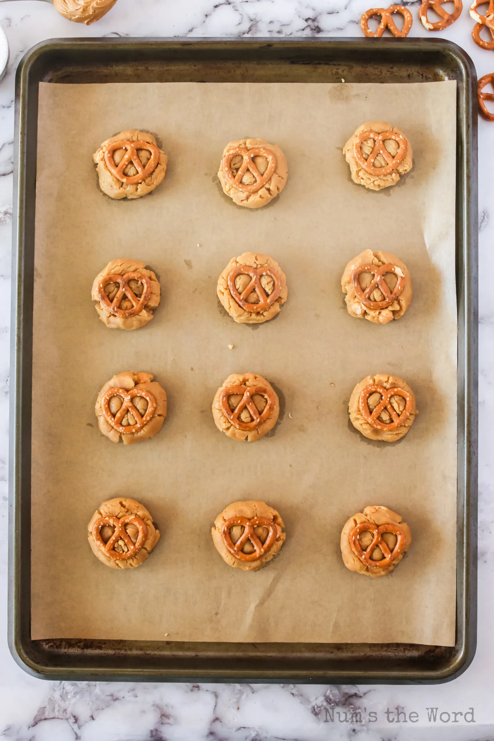 a pretzel pressed into the top of each of the 12 cookies on a cookie sheet