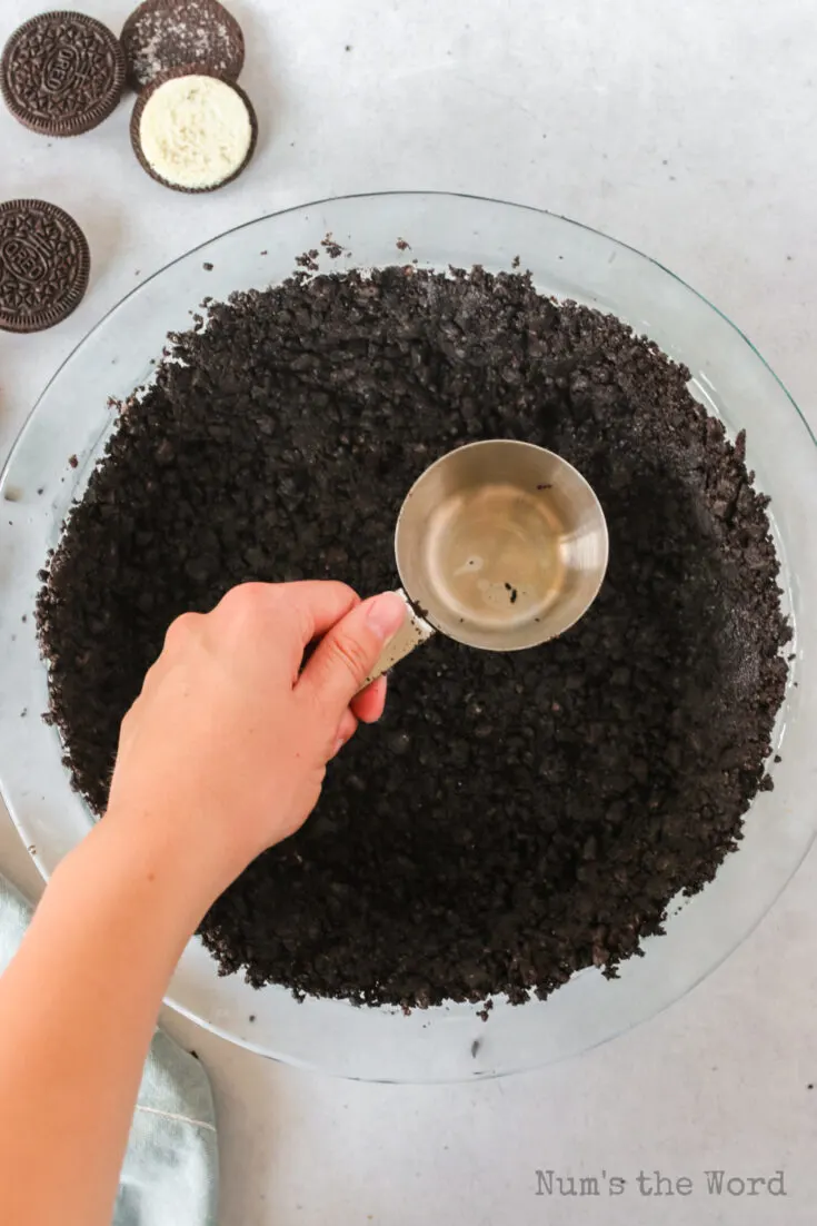 measuring cup pressing cookie crumbs in pie plate