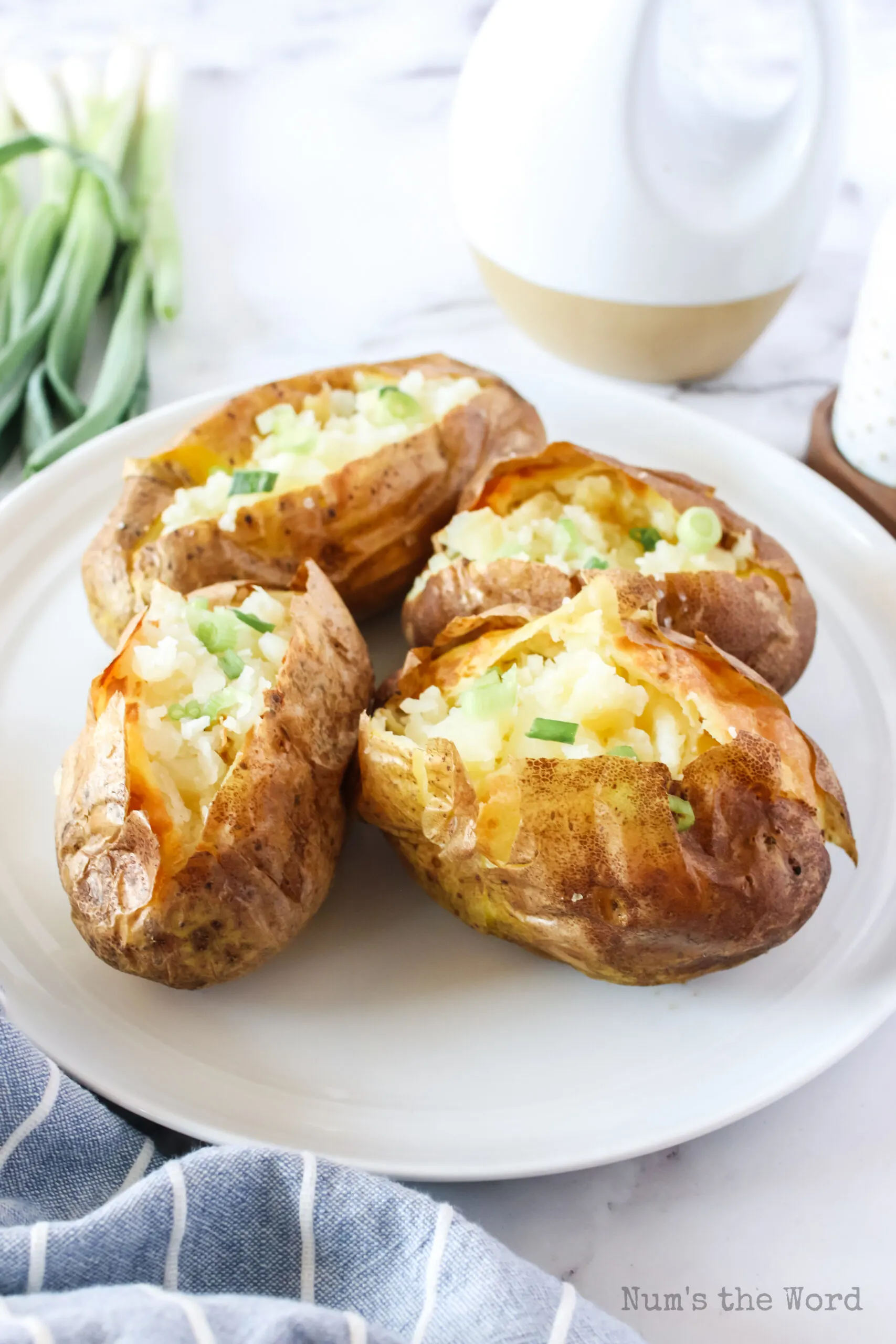 4 baked potatoes on a plate cut open with salt, pepper and green onions.