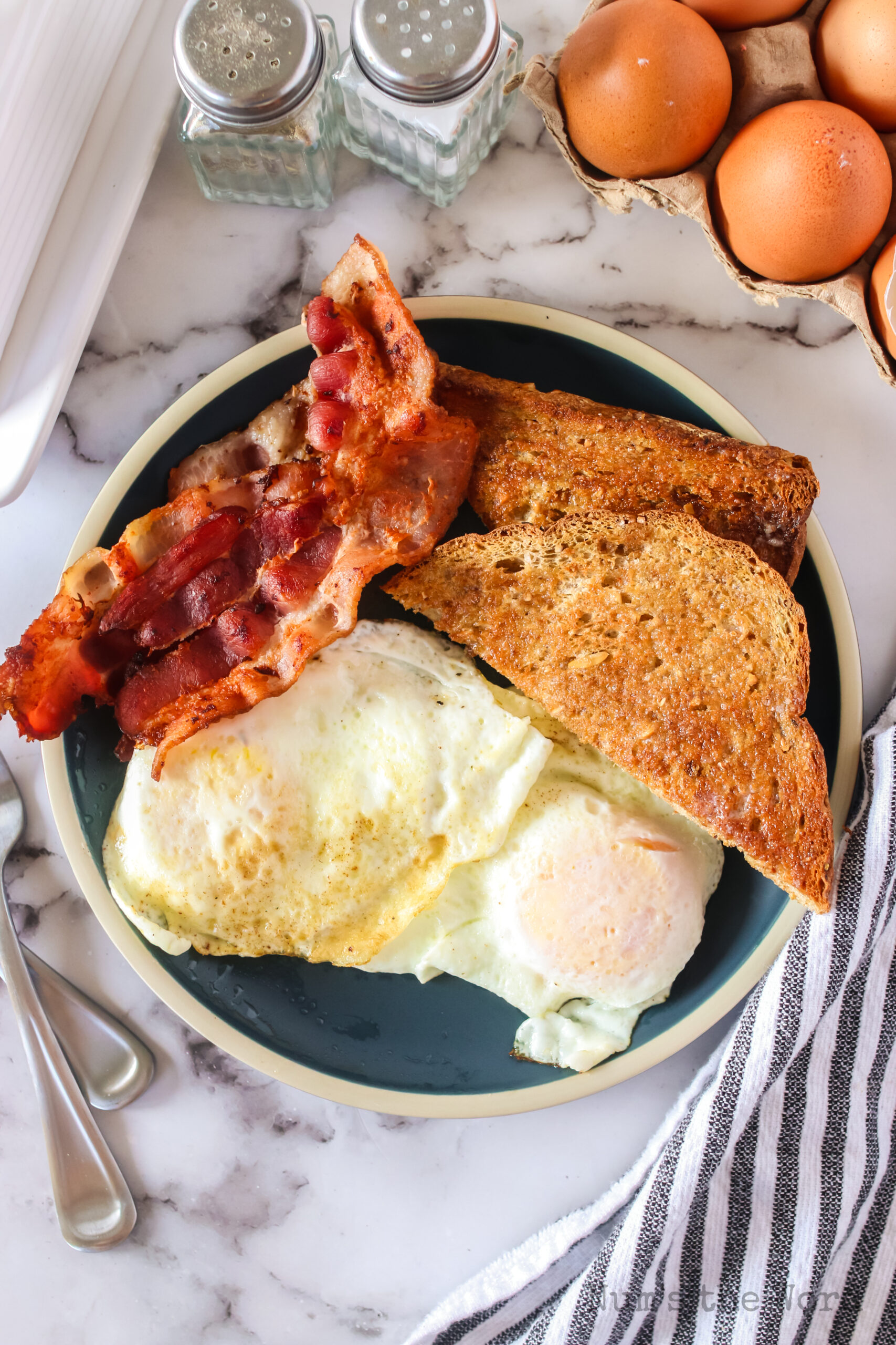 zoomed out image of eggs on plate with toast and bacon