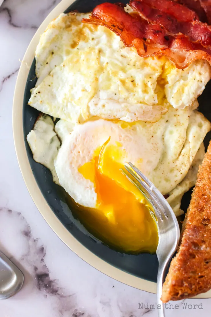 fork breaking egg to show runny yolk