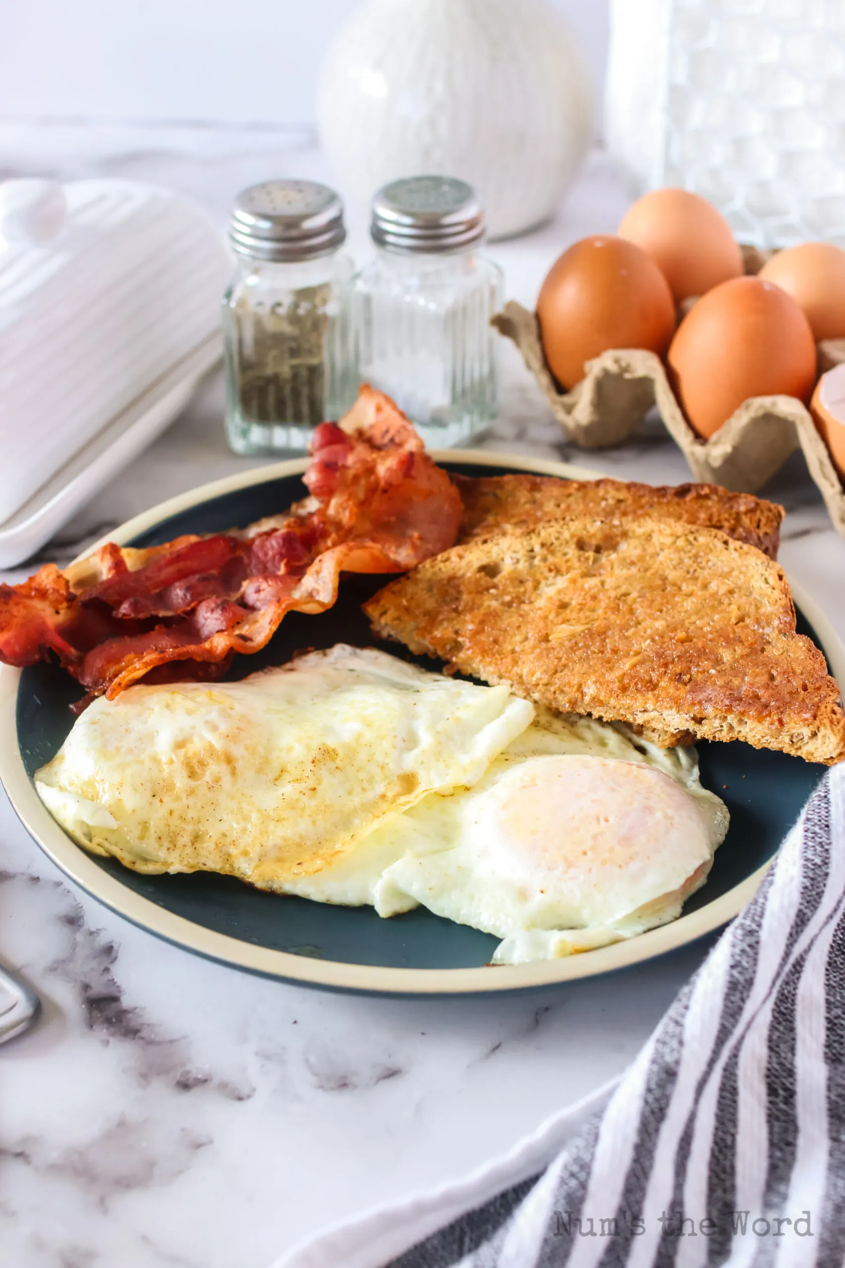 zoomed out side view of eggs on plate with bacon and whole wheat toast