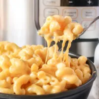 fork scooping a portion of cheesy macaroni and cheese out of a bowl
