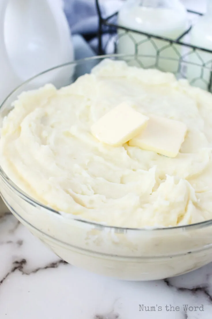 side view of mashed potatoes with garlic in a bowl with two pats of butter ready to serve