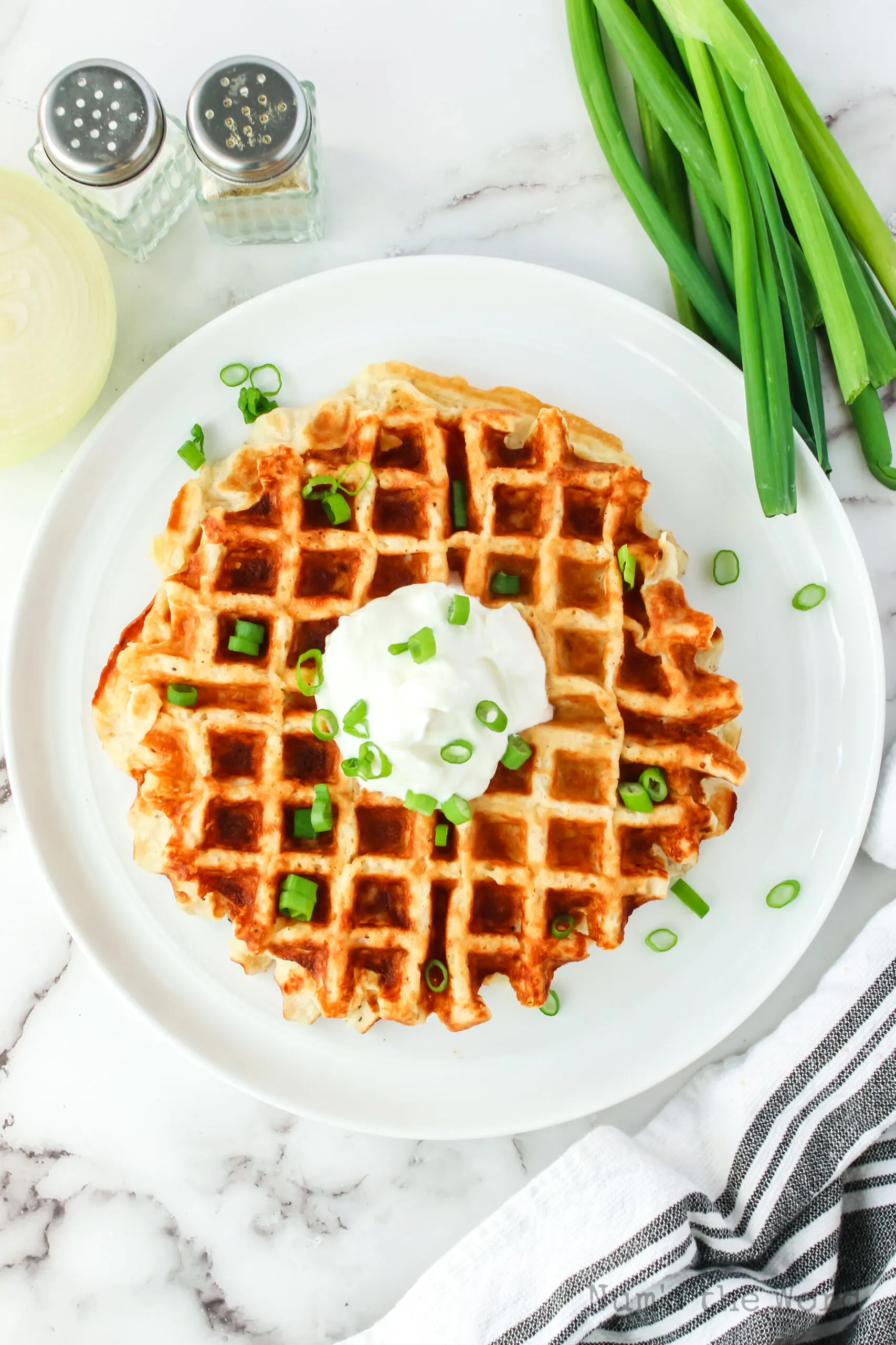 cooked potato waffles on a plate, topped with sour cream and green onions