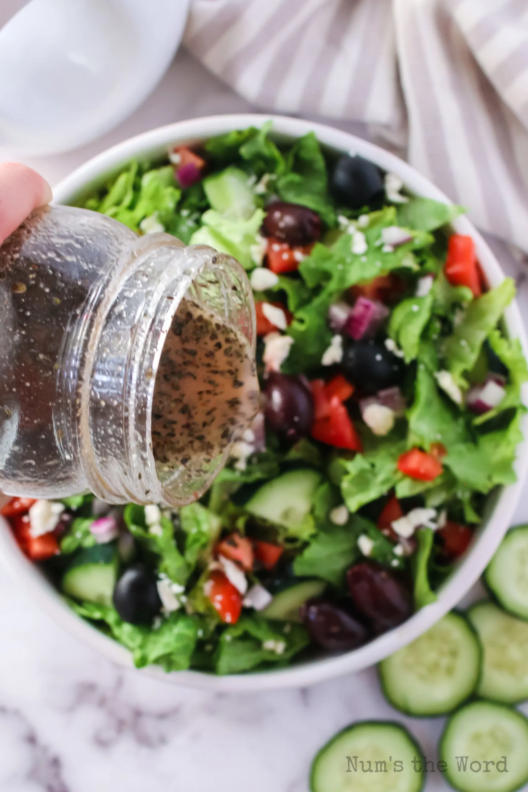 mixed greek salad dressing being poured onto salad