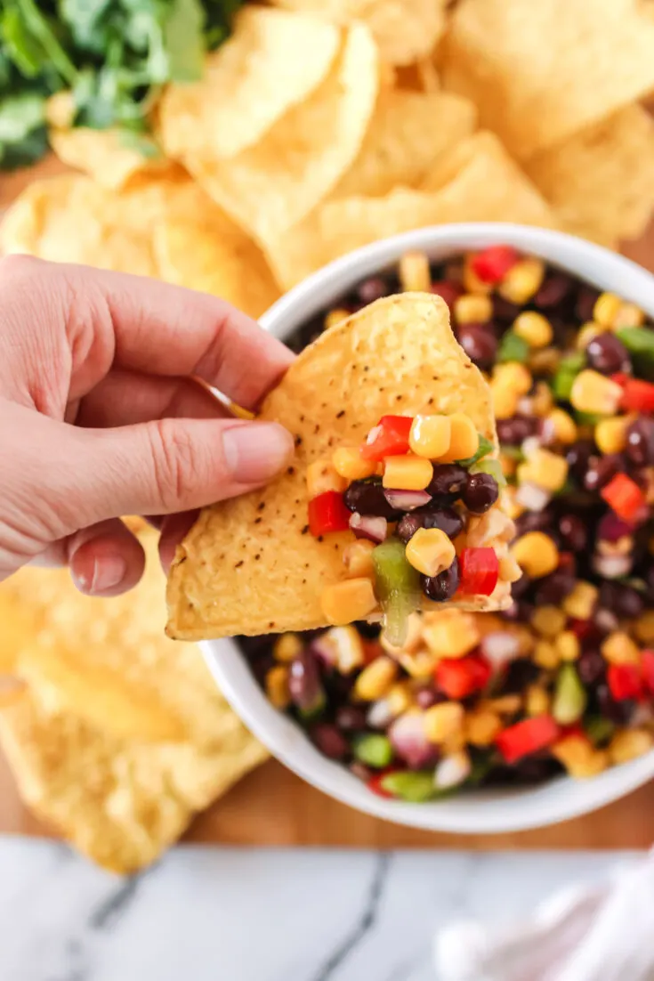 hand holding chip above bowl with black bean salsa on chip.