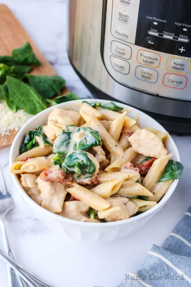 Side view of bowl of creamy tuscan chicken with instant pot in the background.