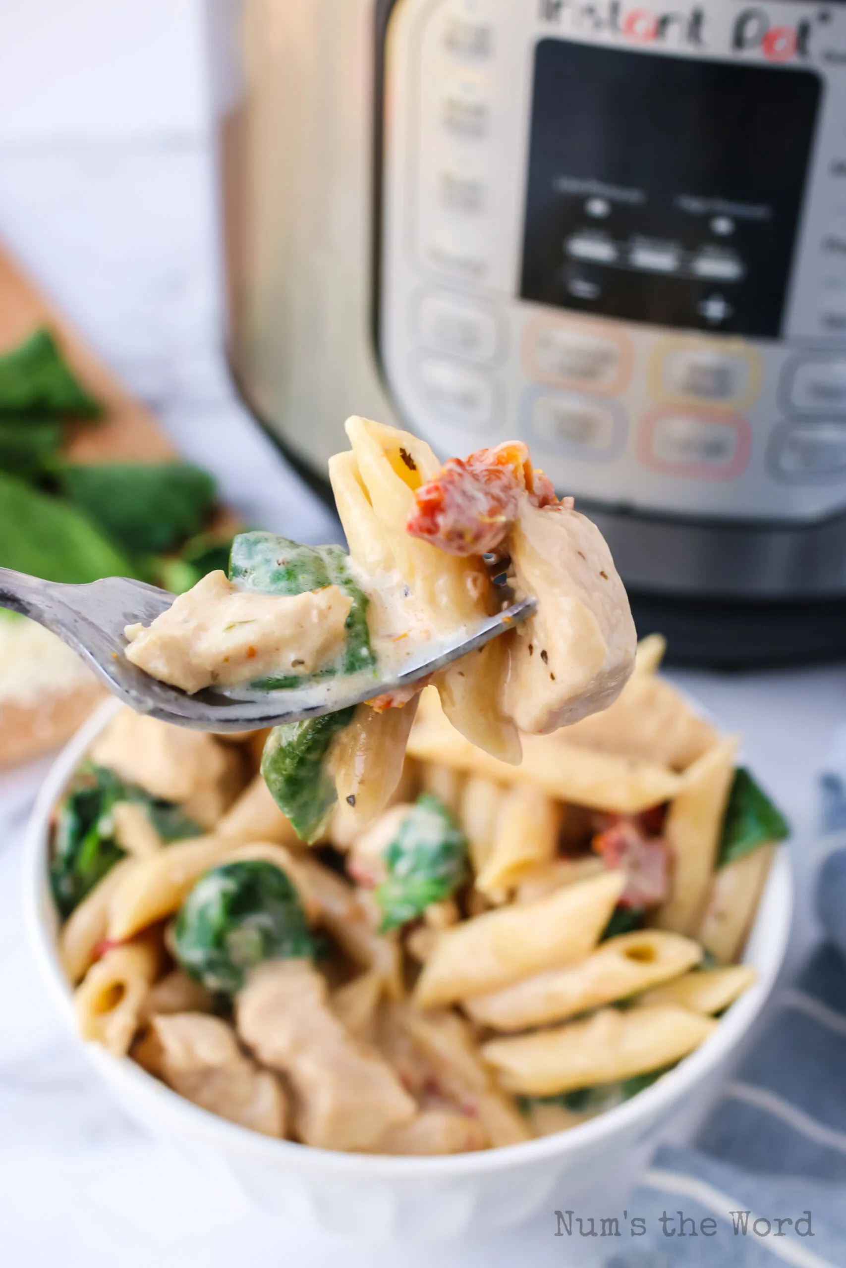 bowl of Tuscan Garlic Chicken in a bowl with instant pot in the back ground. Fork is scooping out a portion.