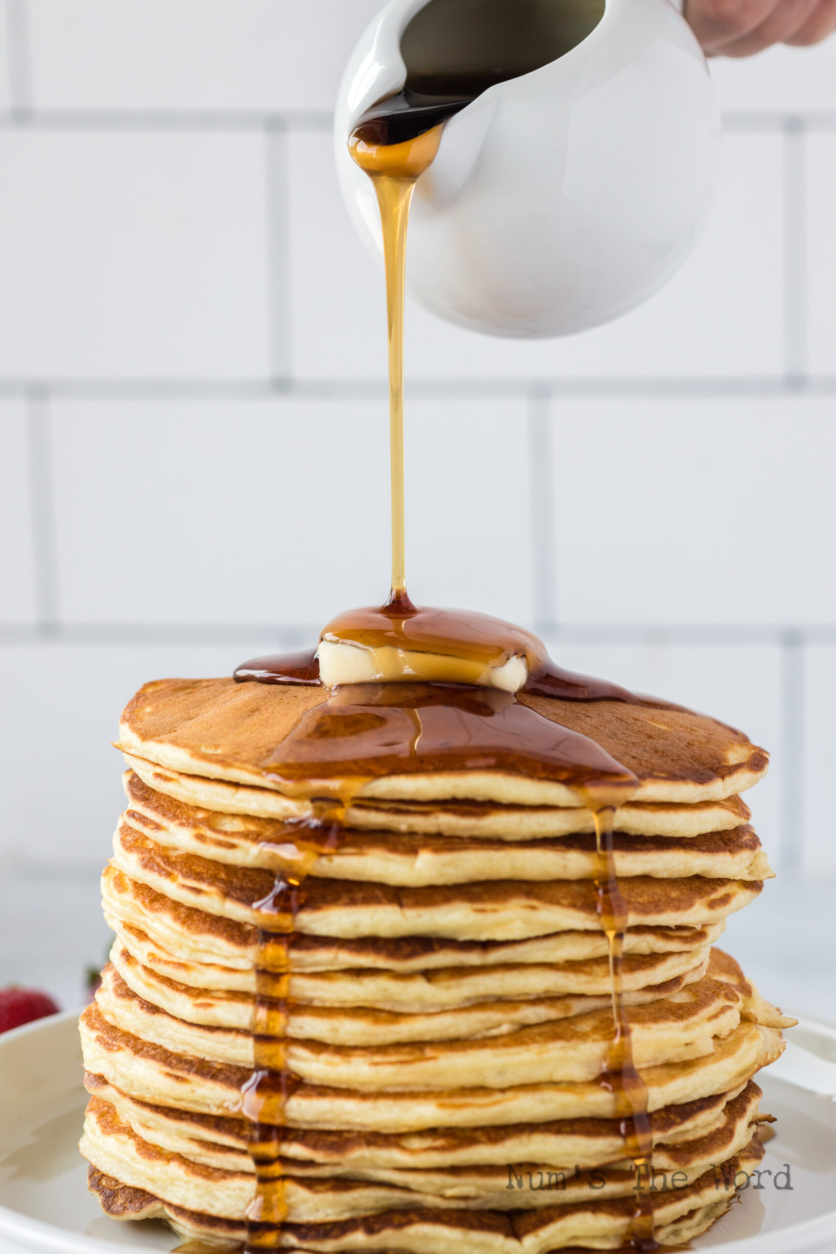 side view of pancakes stacked up with a pat of butter and maple syrup being poured on top