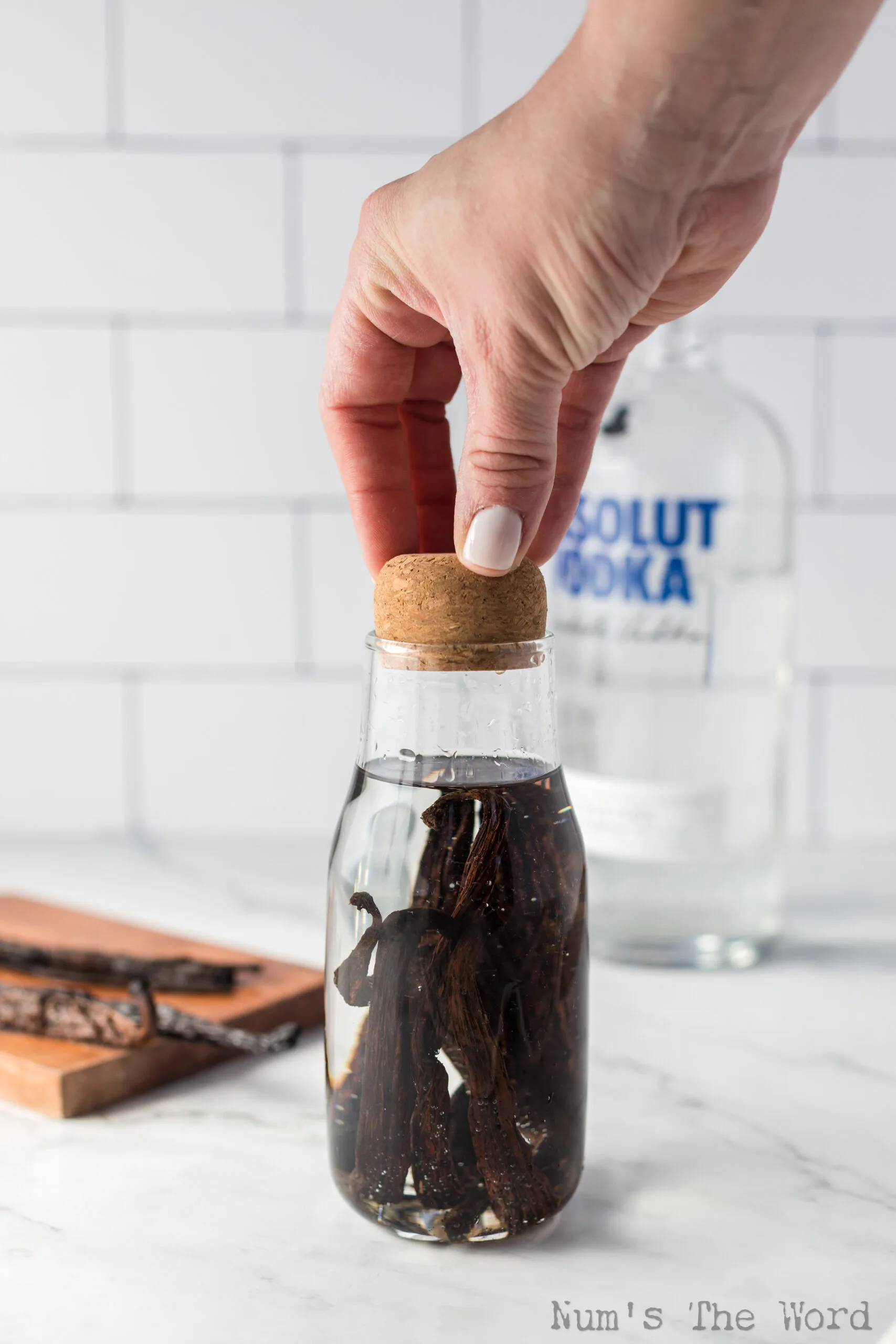 cork cap being placed on glass jar with vanilla beans and vodka.