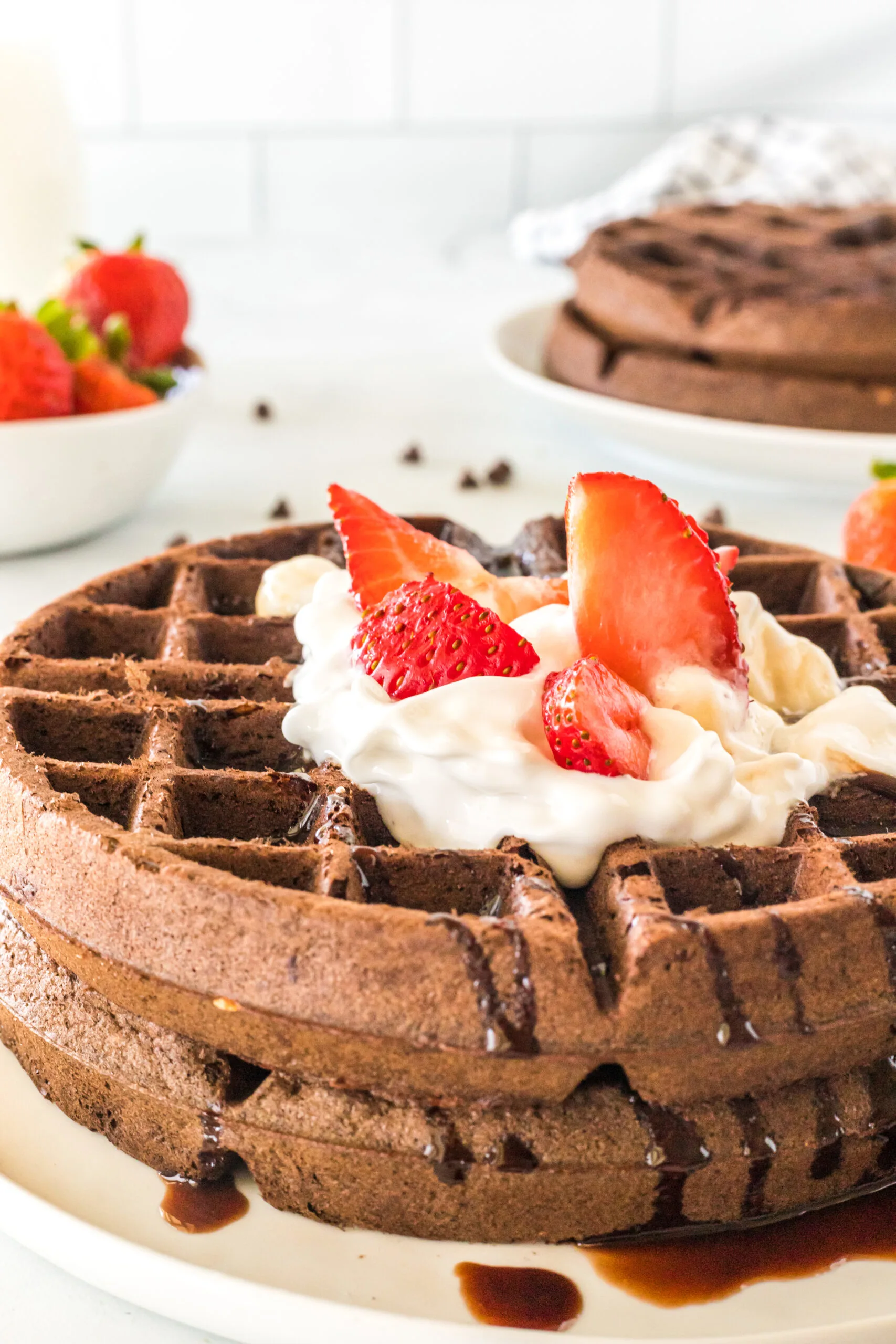 top side view of two chocolate waffles on plate with whipped cream and strawberries