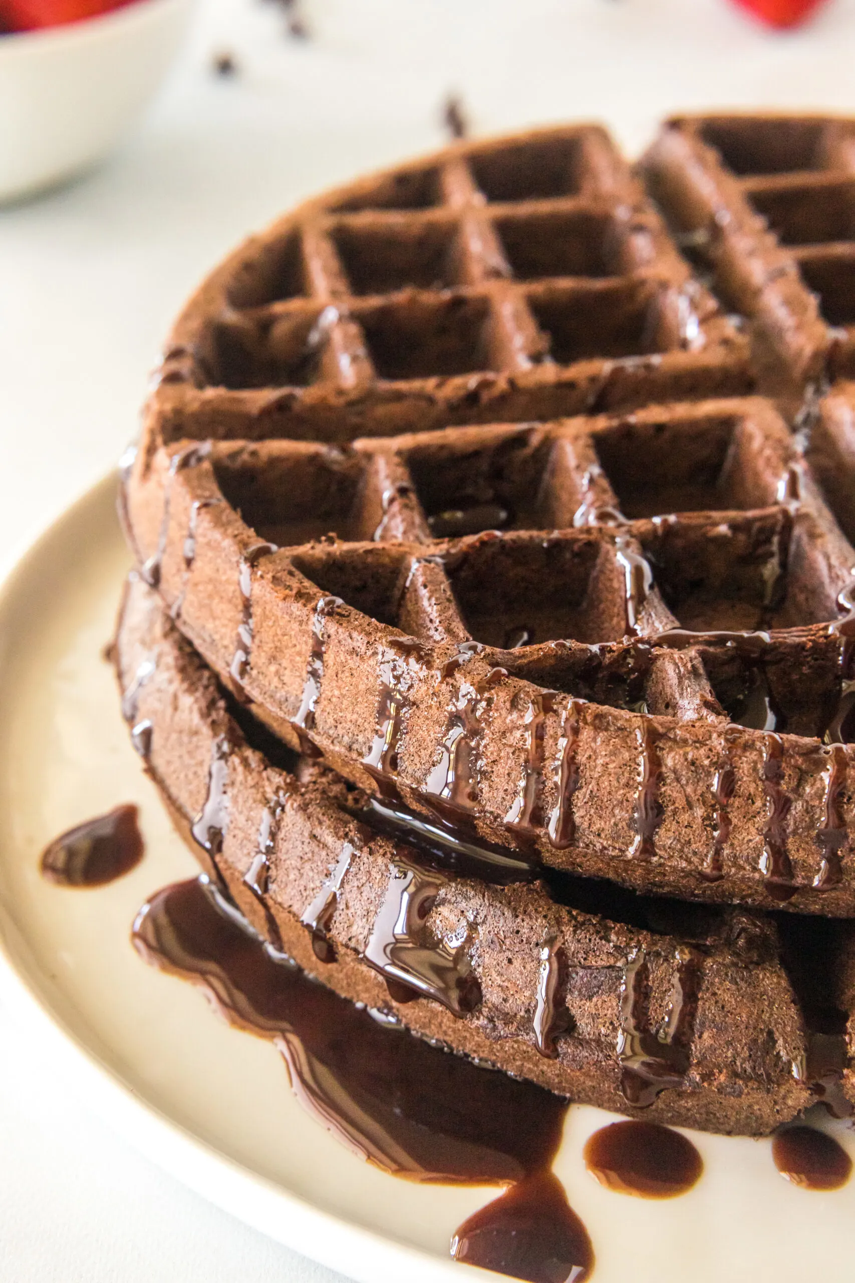 Two chocolate waffles stacked on top of each other with chocolate drizzled on top