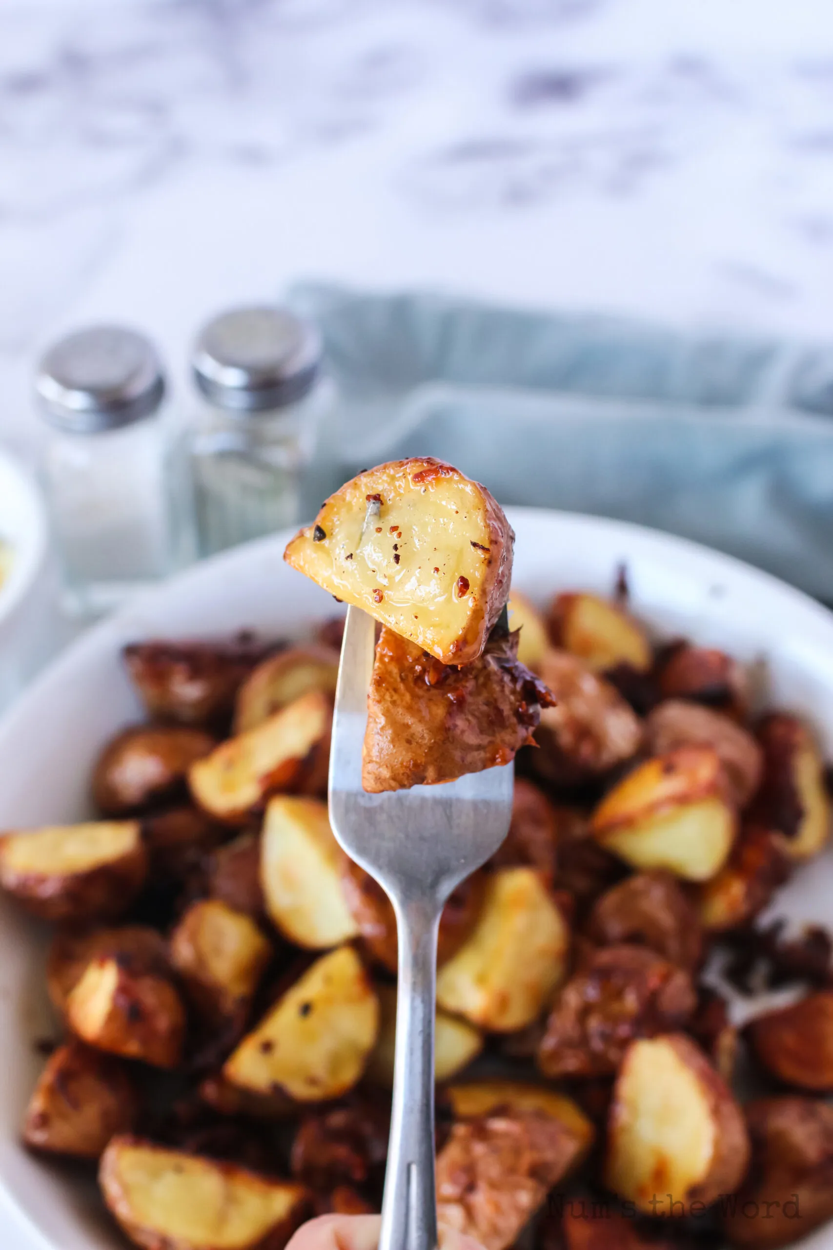 bowl of roasted red potatoes with a fork pricking two and holding them above the bowl.