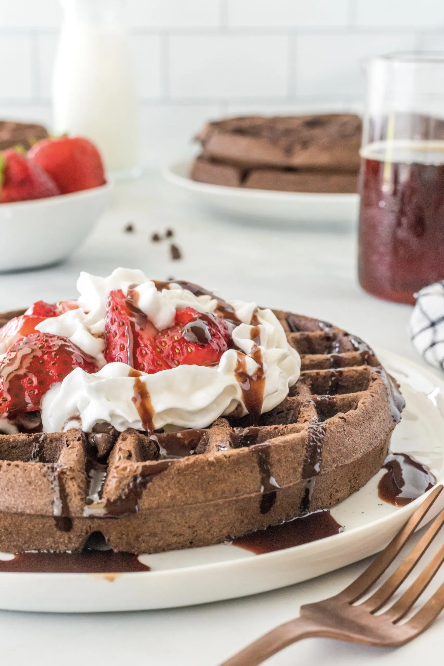 side view of single waffle with strawberries, whipped cream and chocolate syrup