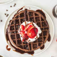 top view looking down at chocolate waffle topped with whipped cream, strawberries and chocolate syrup